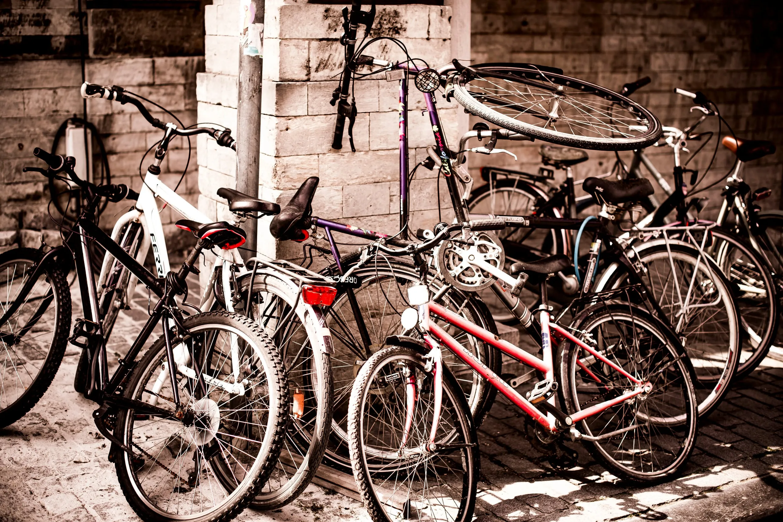 A tangle of parked bicycles against a brick wall, in warm sepia tones