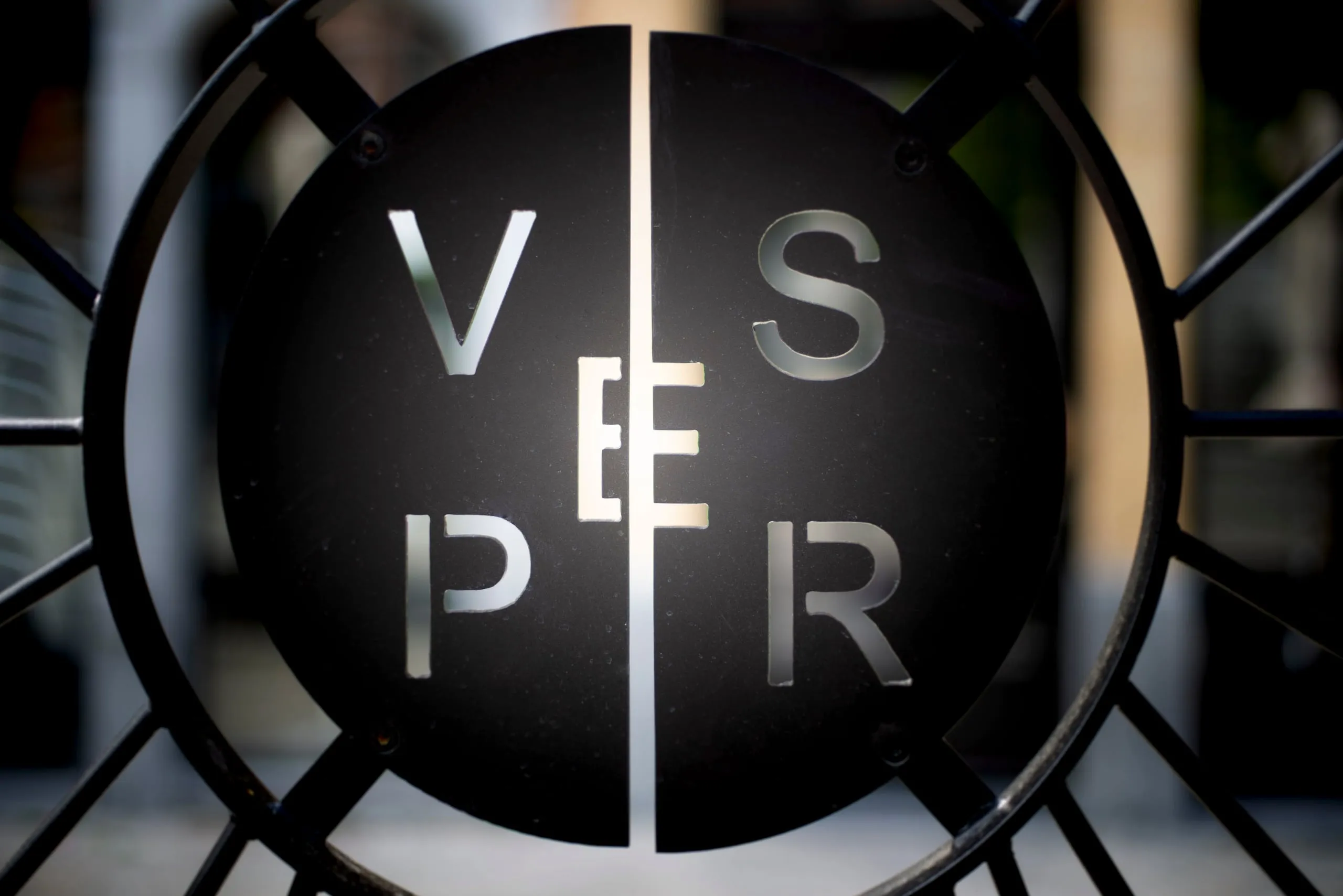 Wrought-iron gate with a round sign bearing the letters of Vesper