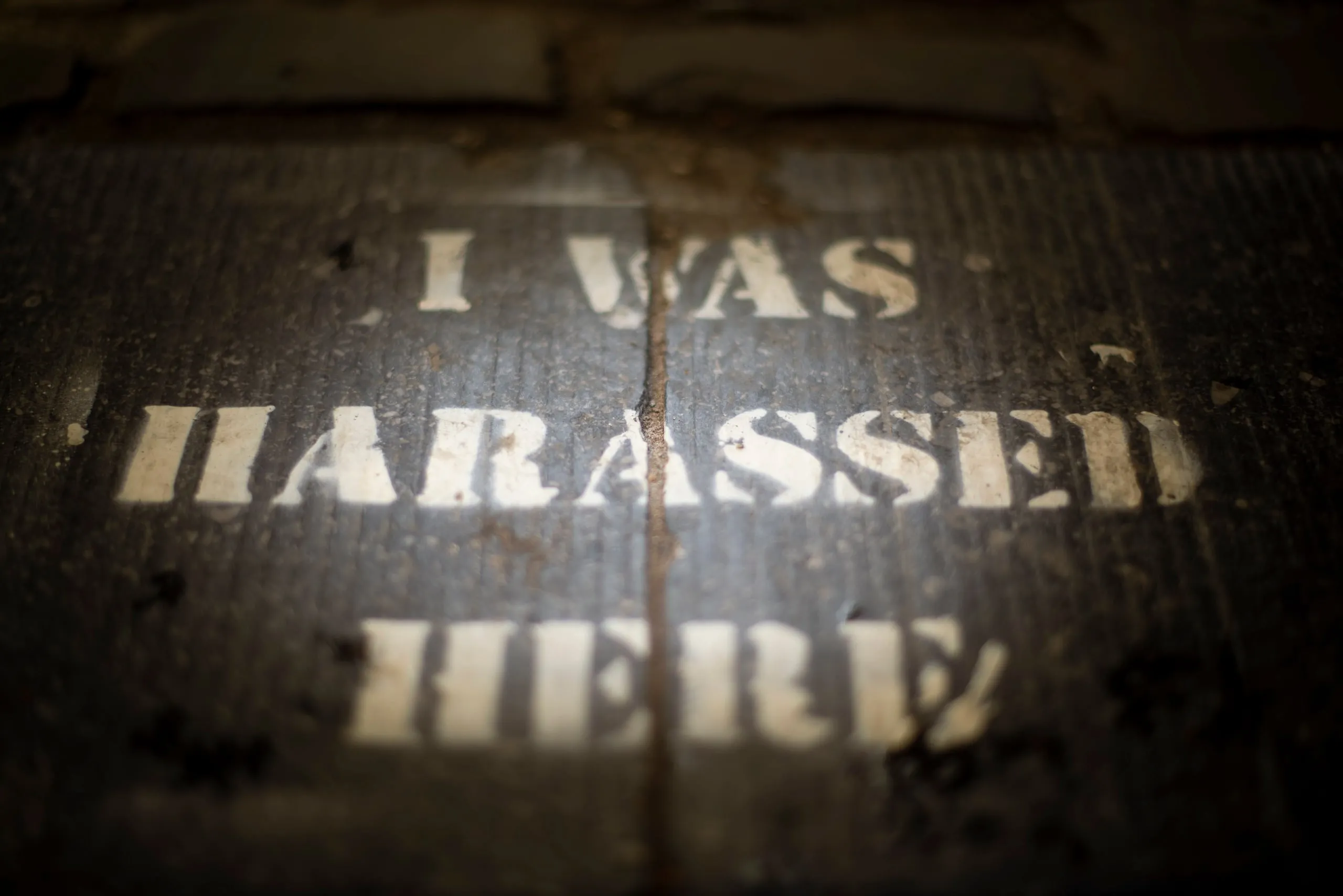Stencilled text 'I was harassed here' on a dark pavement