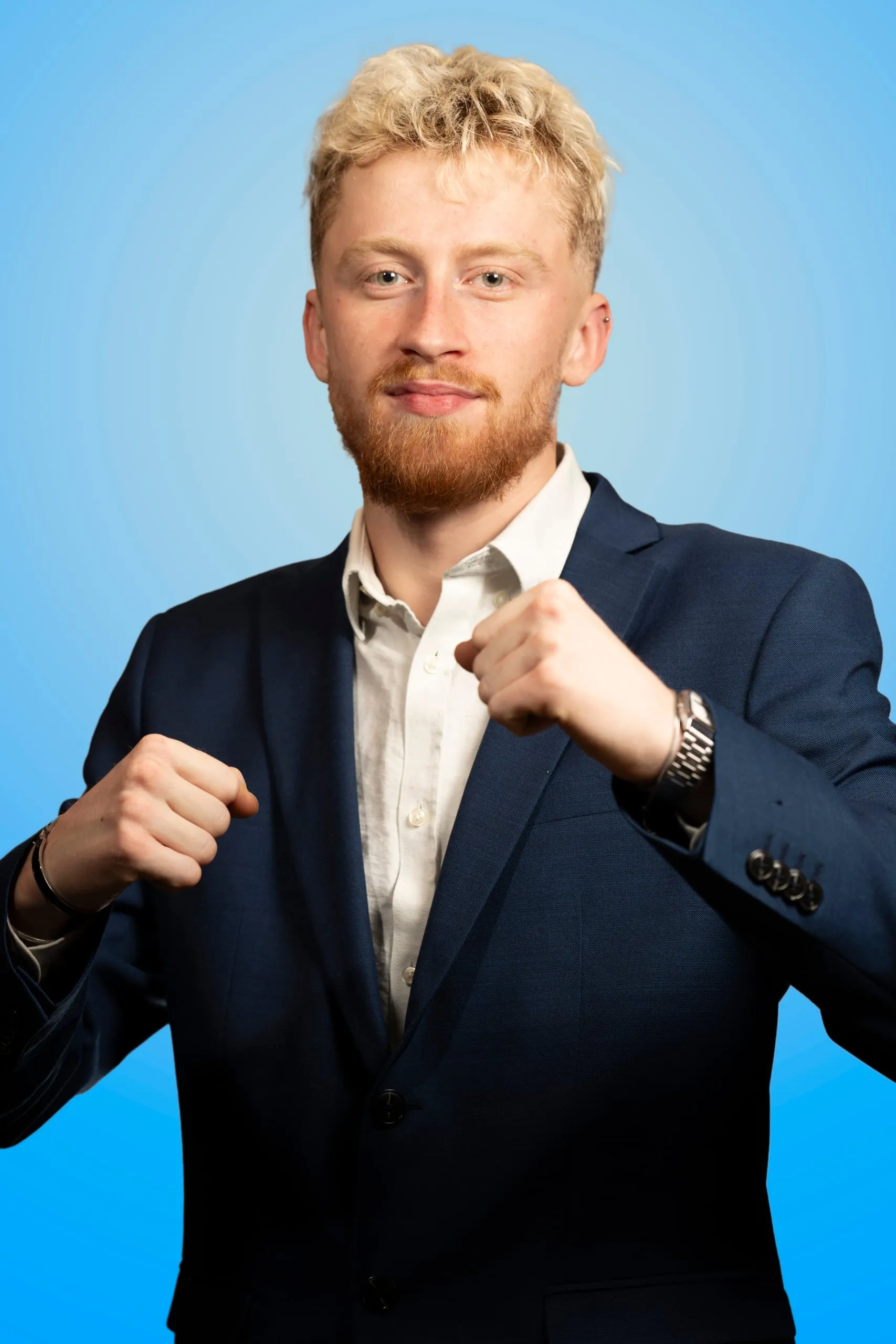 Man in a navy suit with clenched fists against a blue background