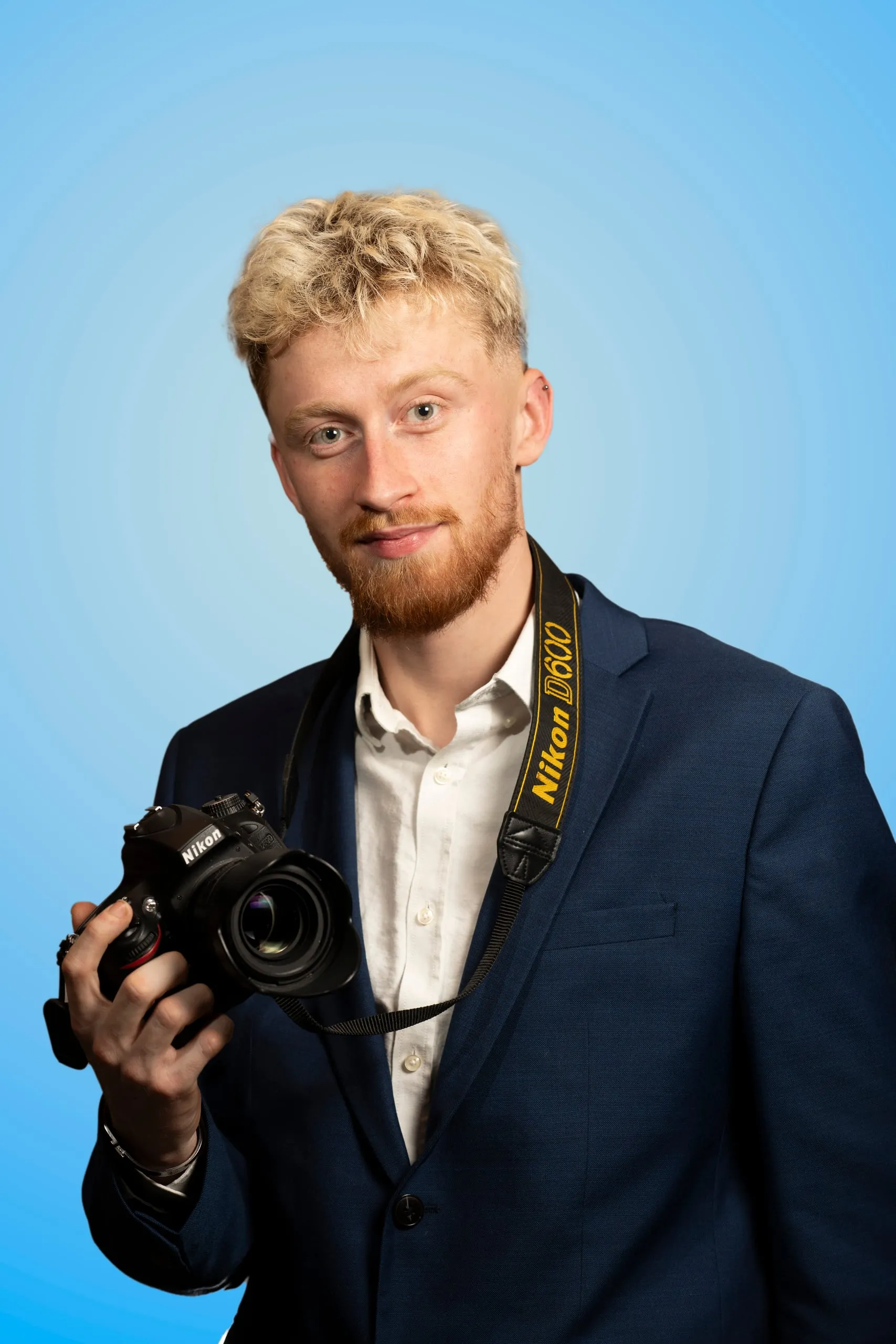 Man in a navy suit holding a camera against a blue background
