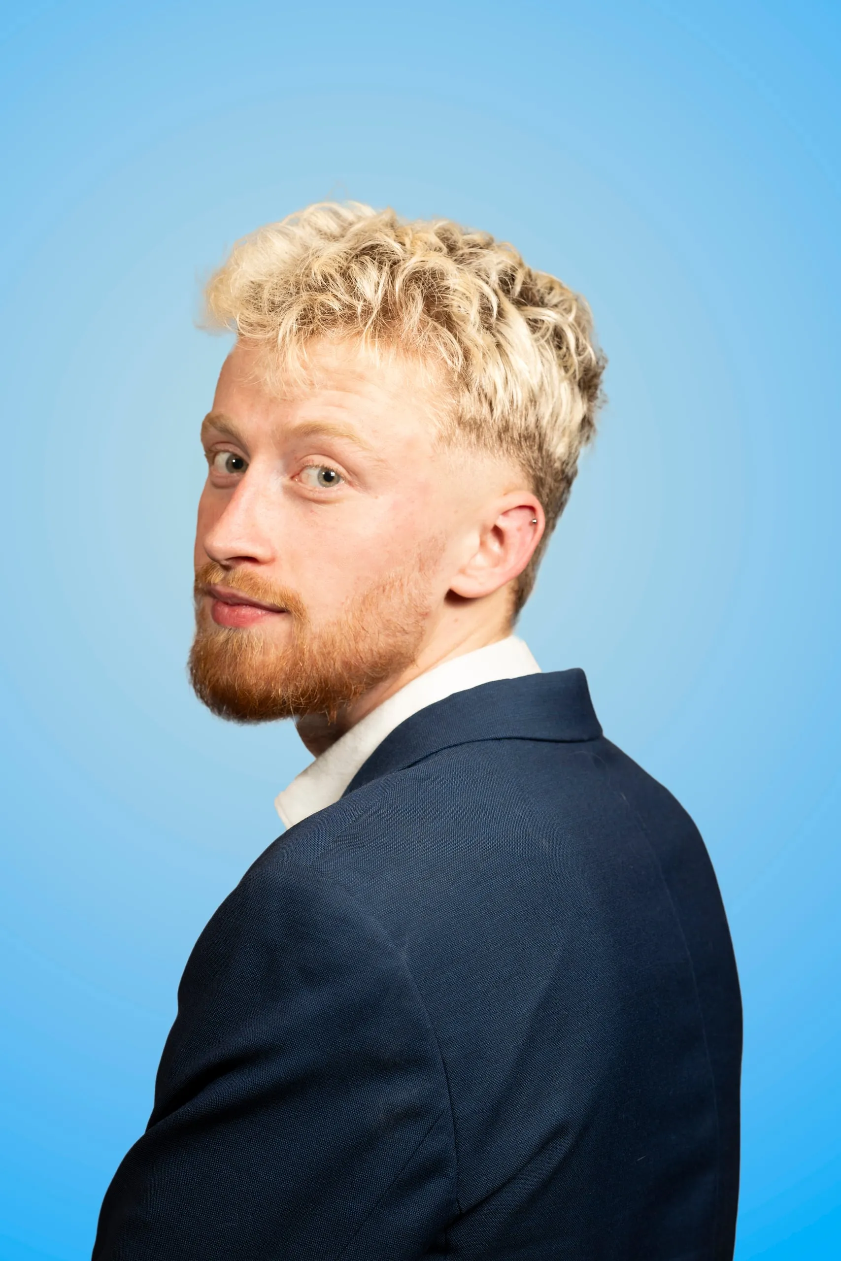 Man in a navy suit looks over his shoulder at the camera