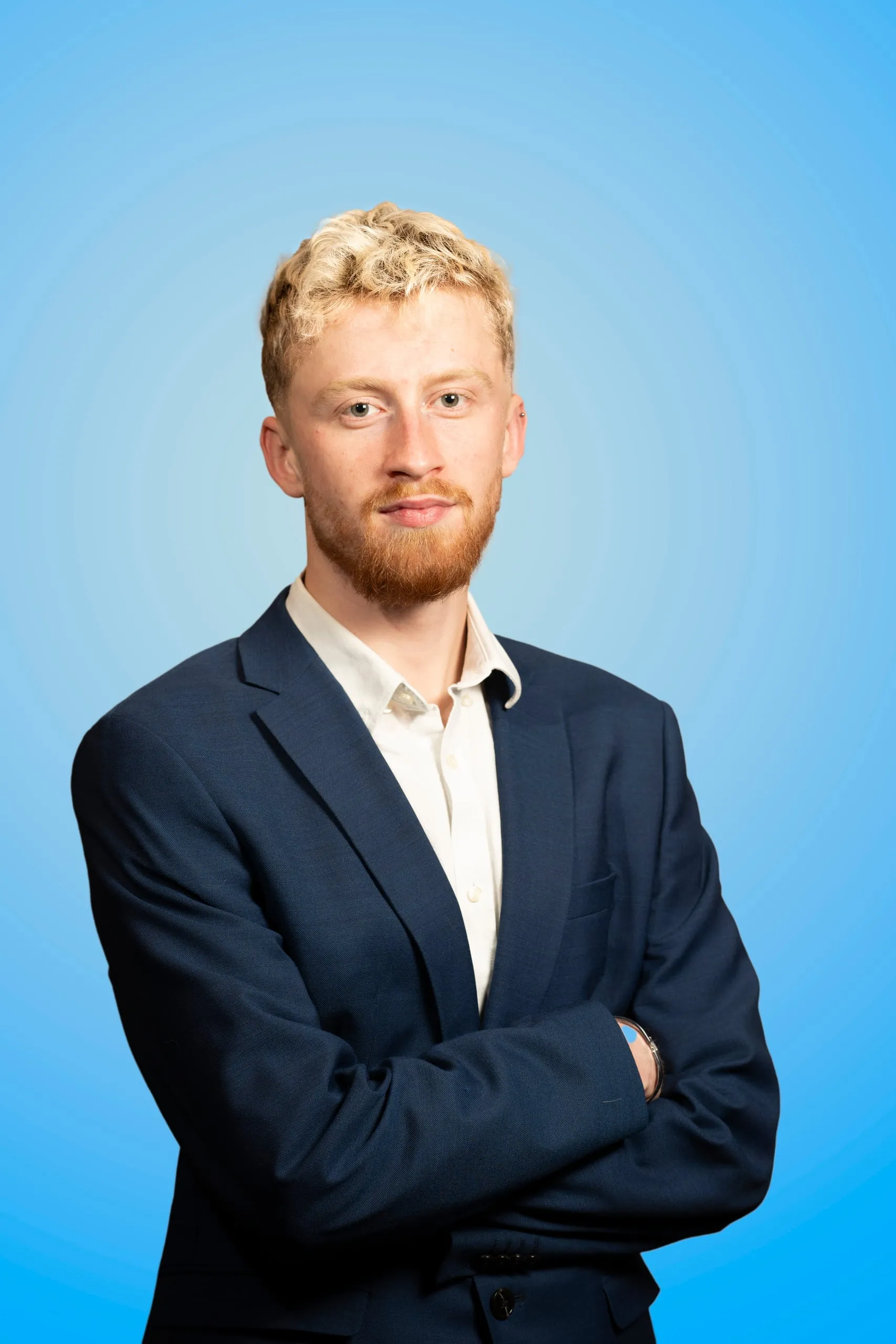 Man in a navy suit with his arms crossed against a blue background