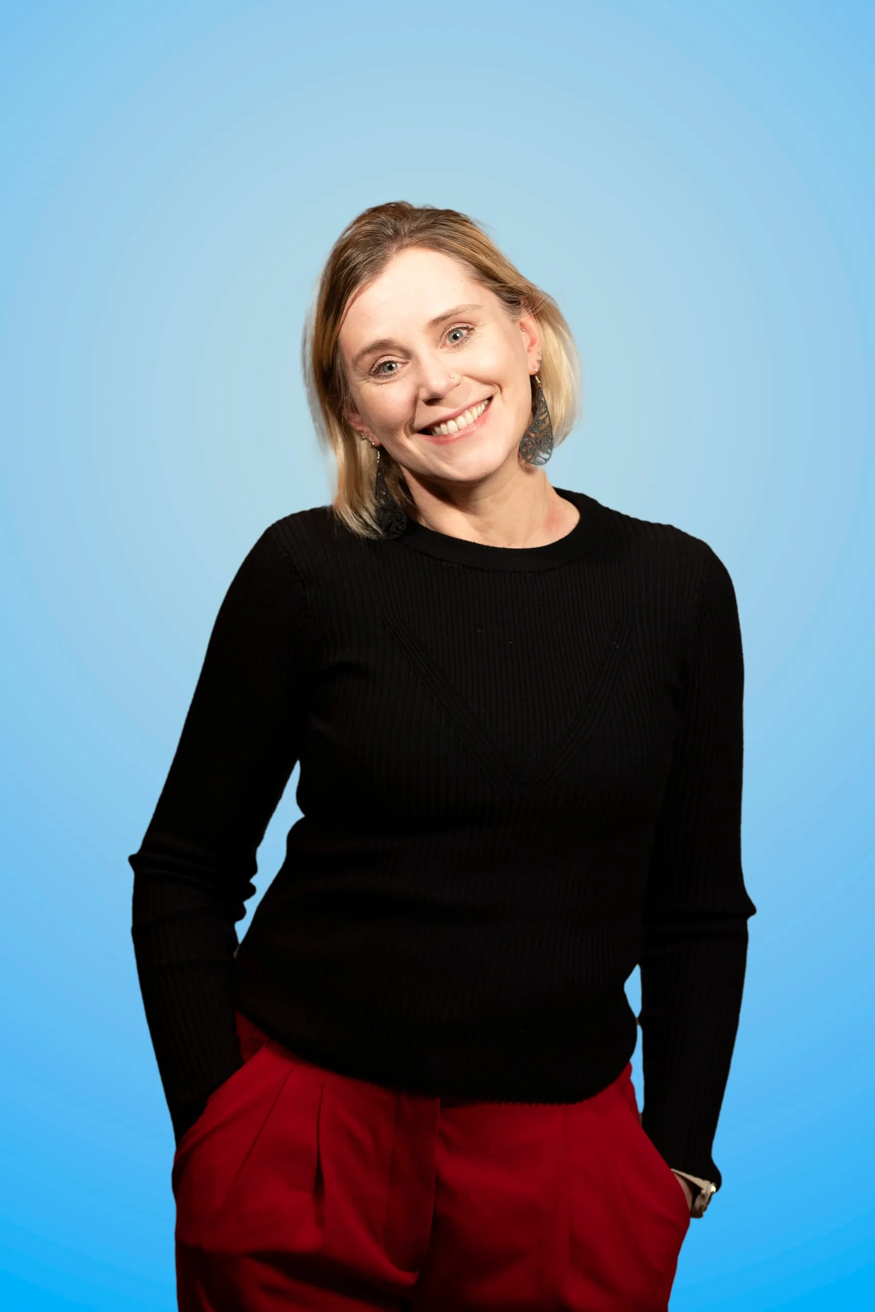 Smiling woman in a black sweater and red trousers with one hand in her pocket