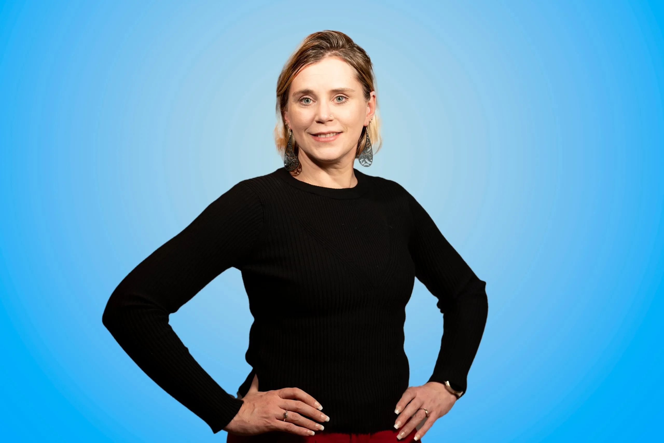 Woman in a black sweater with her hands on her hips against a blue background