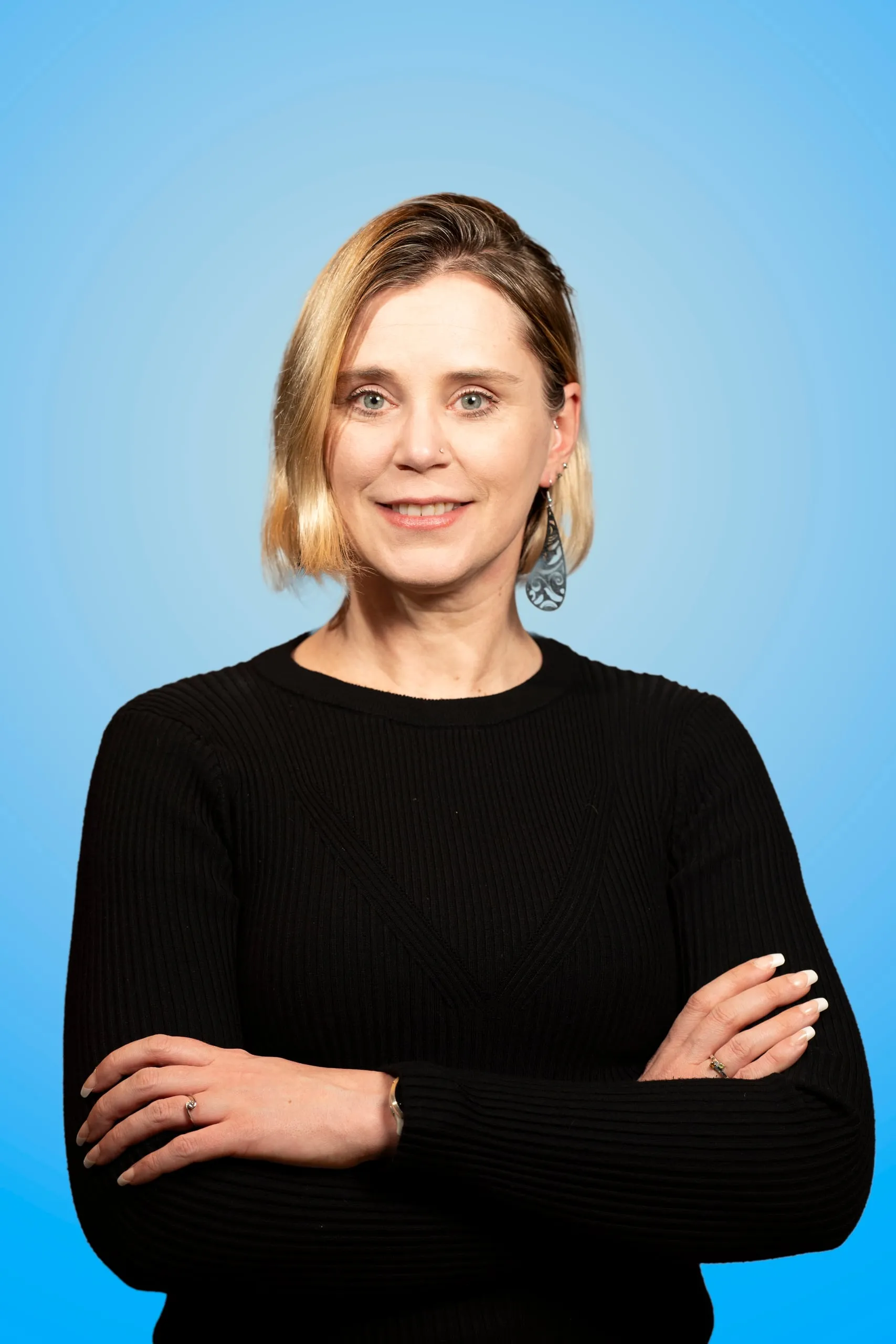 Woman in a black sweater with her arms crossed against a blue background