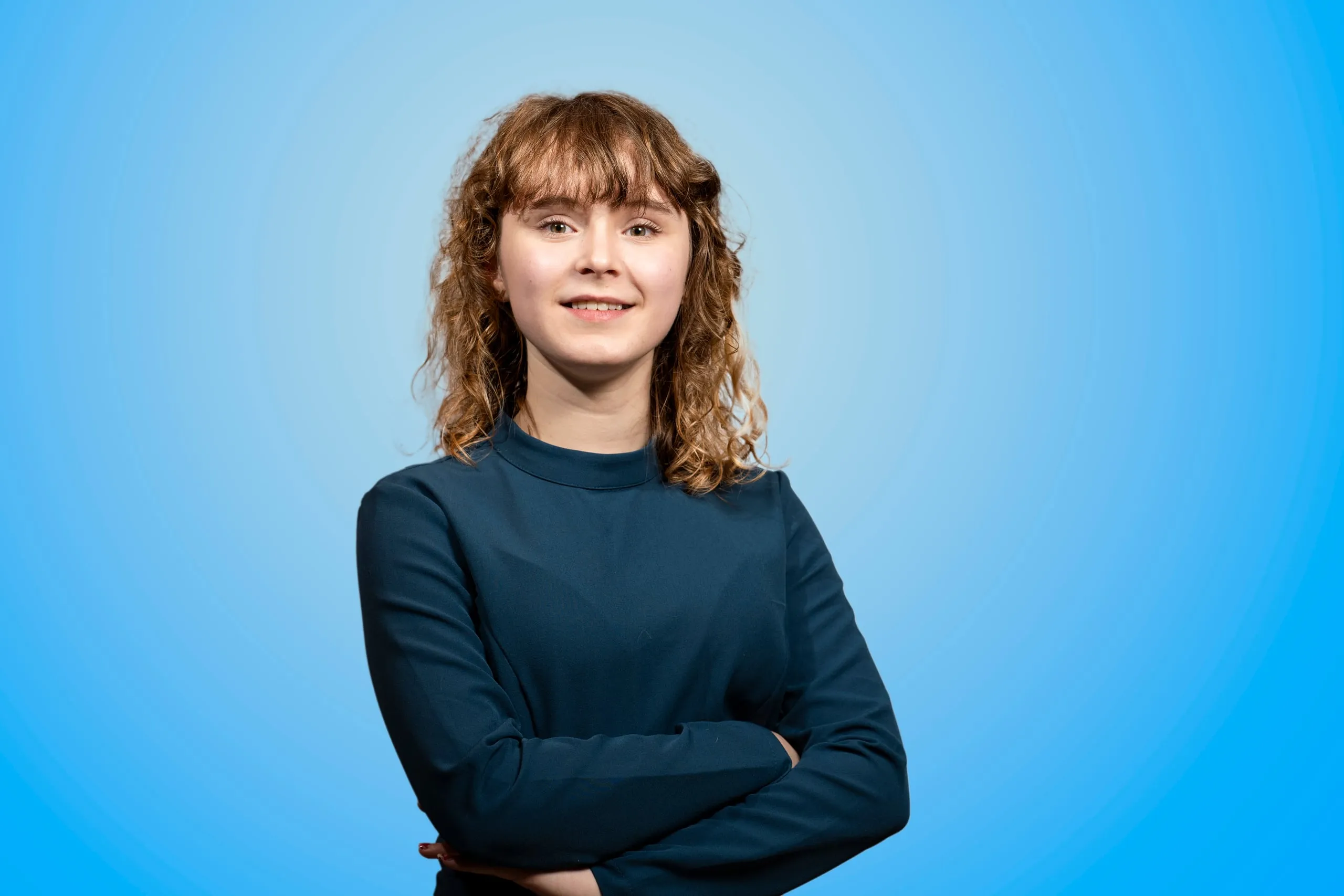 Young woman with curly hair in a blue dress with her arms crossed