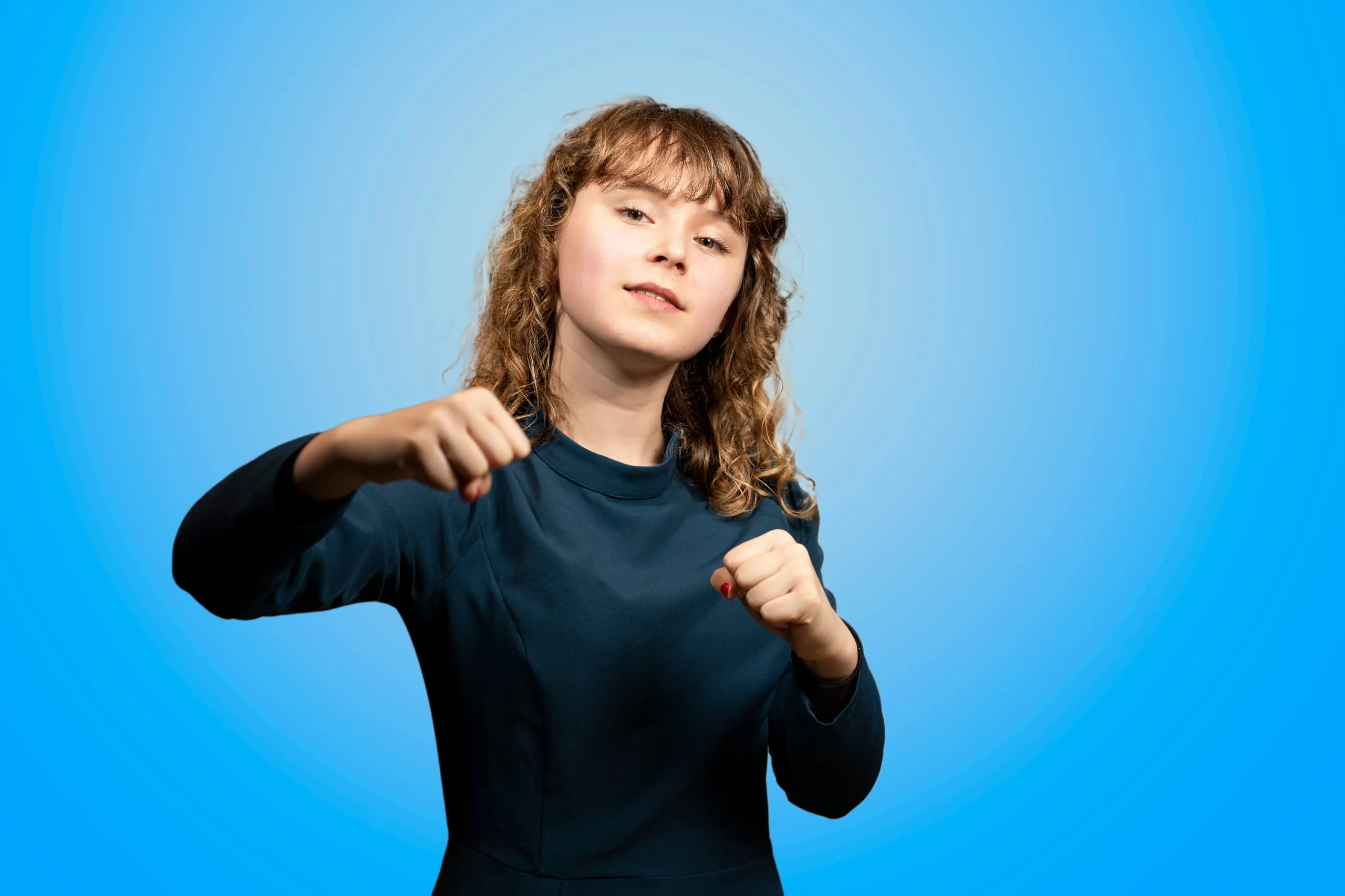 Young woman with curly hair in a blue dress with clenched fists in a playful pose