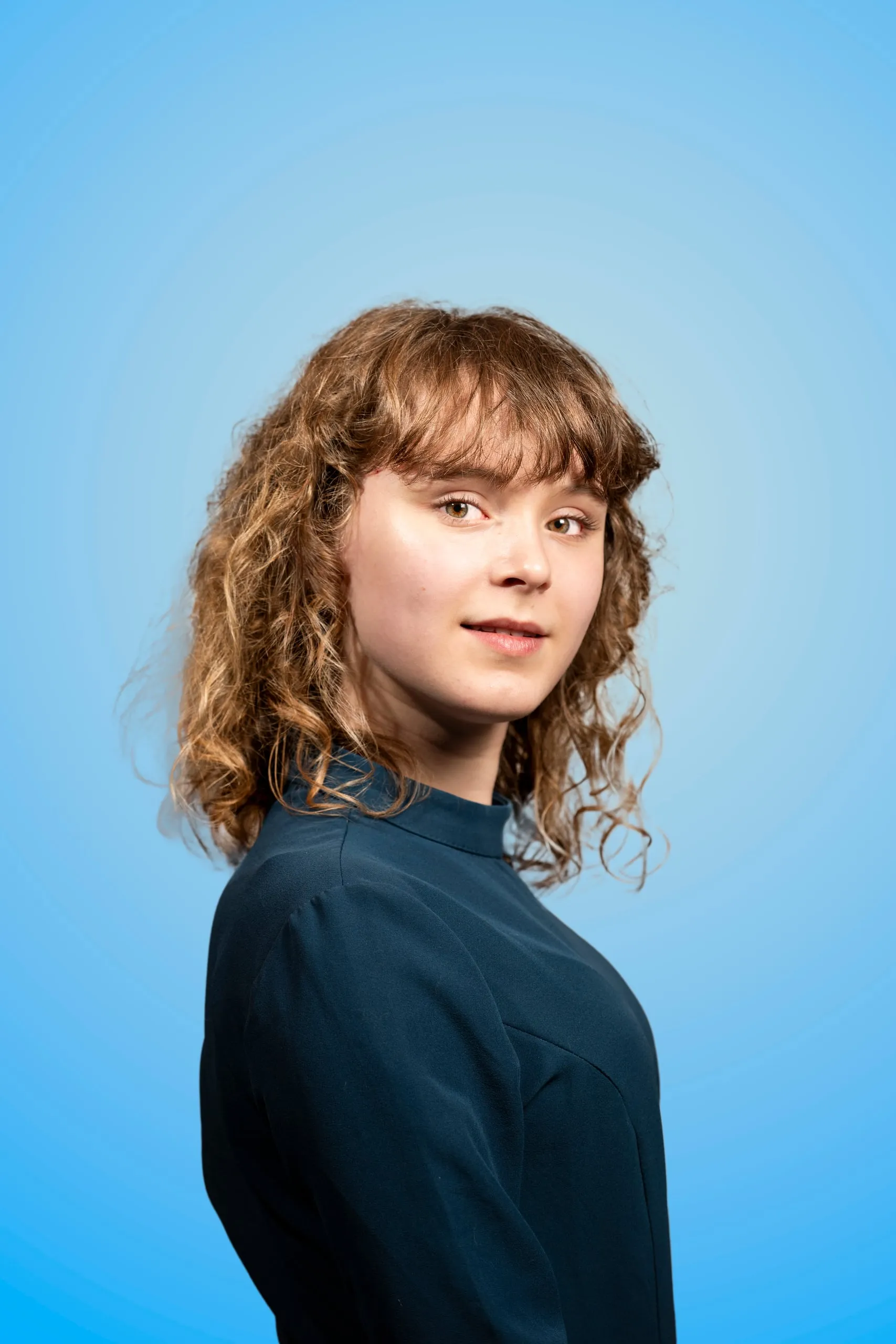 Young woman with curly hair looks over her shoulder at the camera