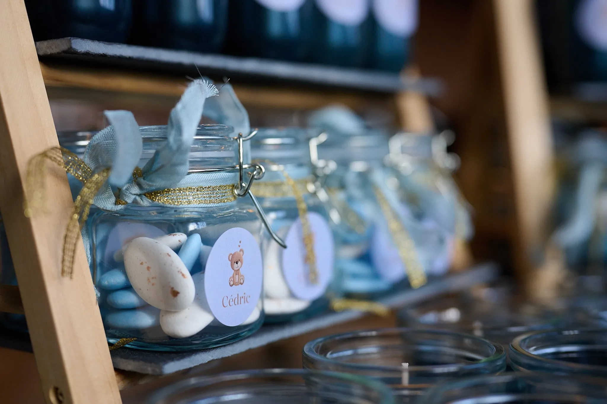 Glass jars with blue sugared almonds and a ribbon on a wooden rack