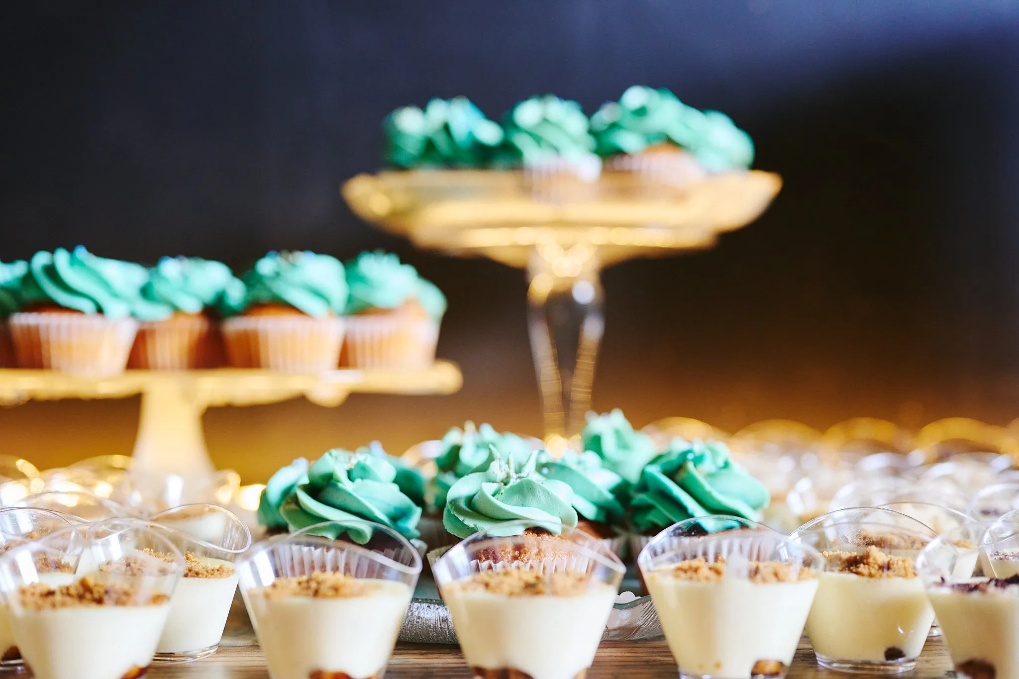 Cupcakes with mint-green topping and dessert glasses on cake stands