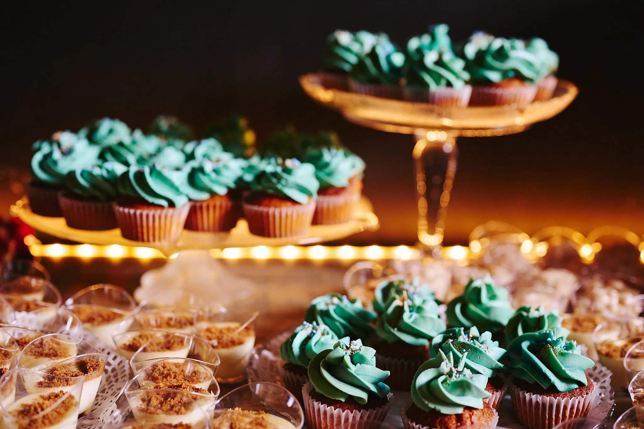 Warmly lit dessert buffet with cupcakes and dessert glasses