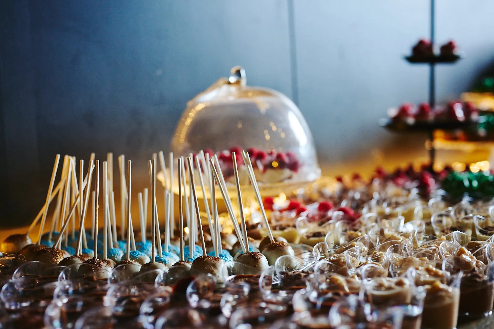 Buffet with cake pops and dessert glasses under a glass dome
