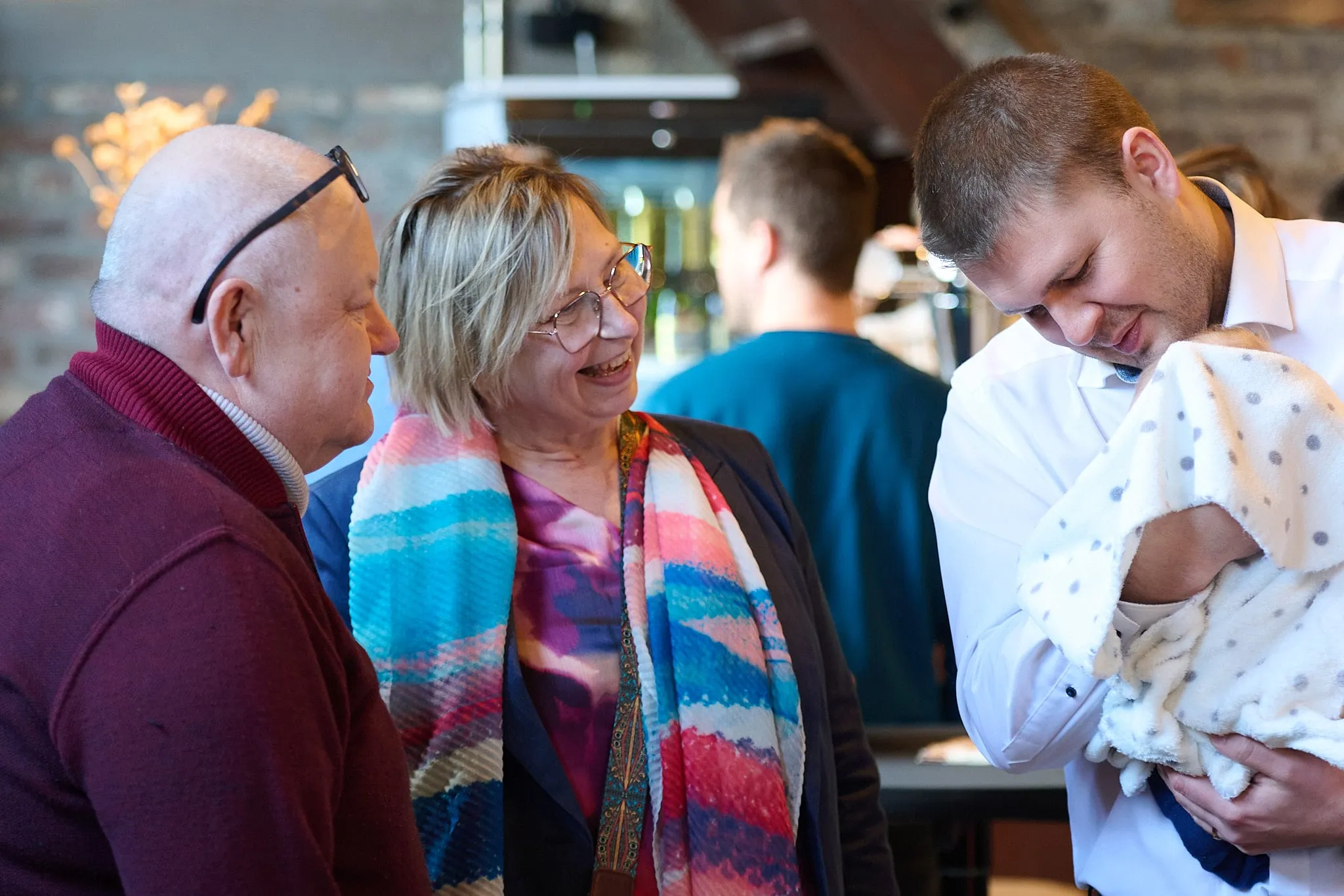 Guests in conversation, a man on the right holding a baby