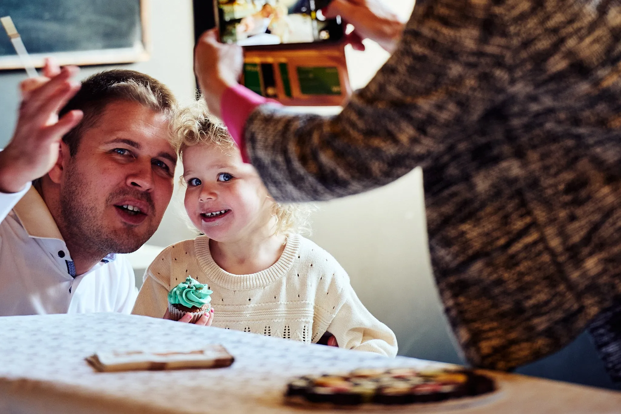 Father and toddler laugh while someone takes a photo with a phone