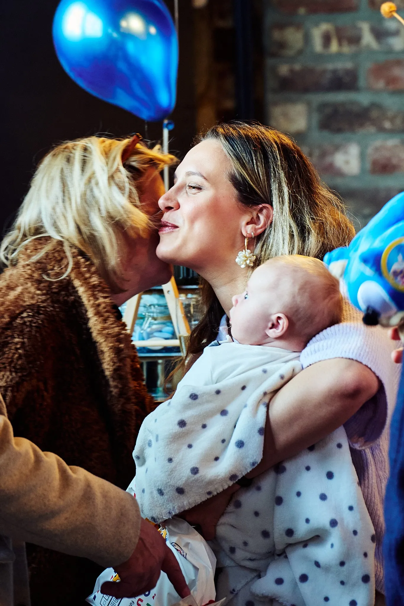 A guest kisses a young mother with a baby on the cheek