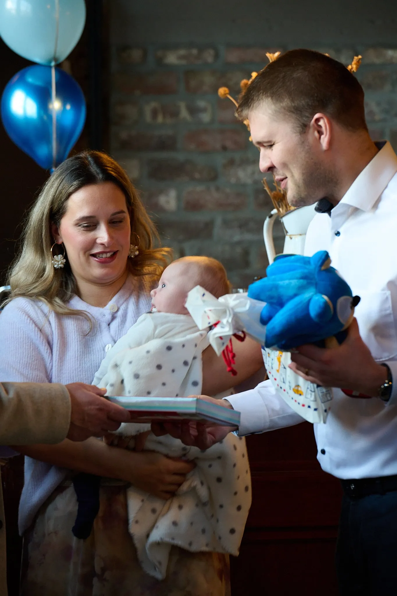 A man hands a blue cuddly toy to a woman with a baby