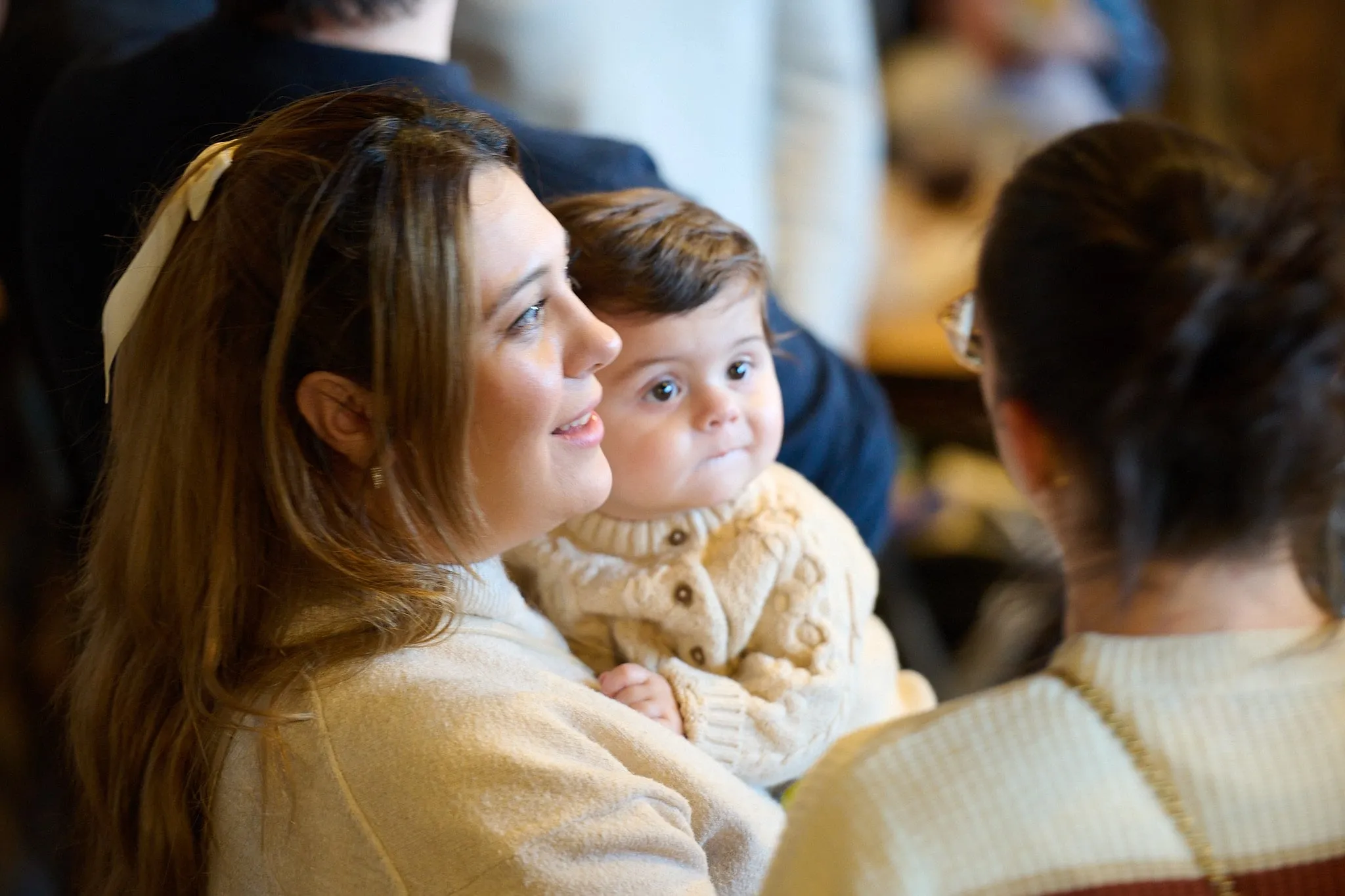 Woman with a toddler on her lap looks aside among other guests