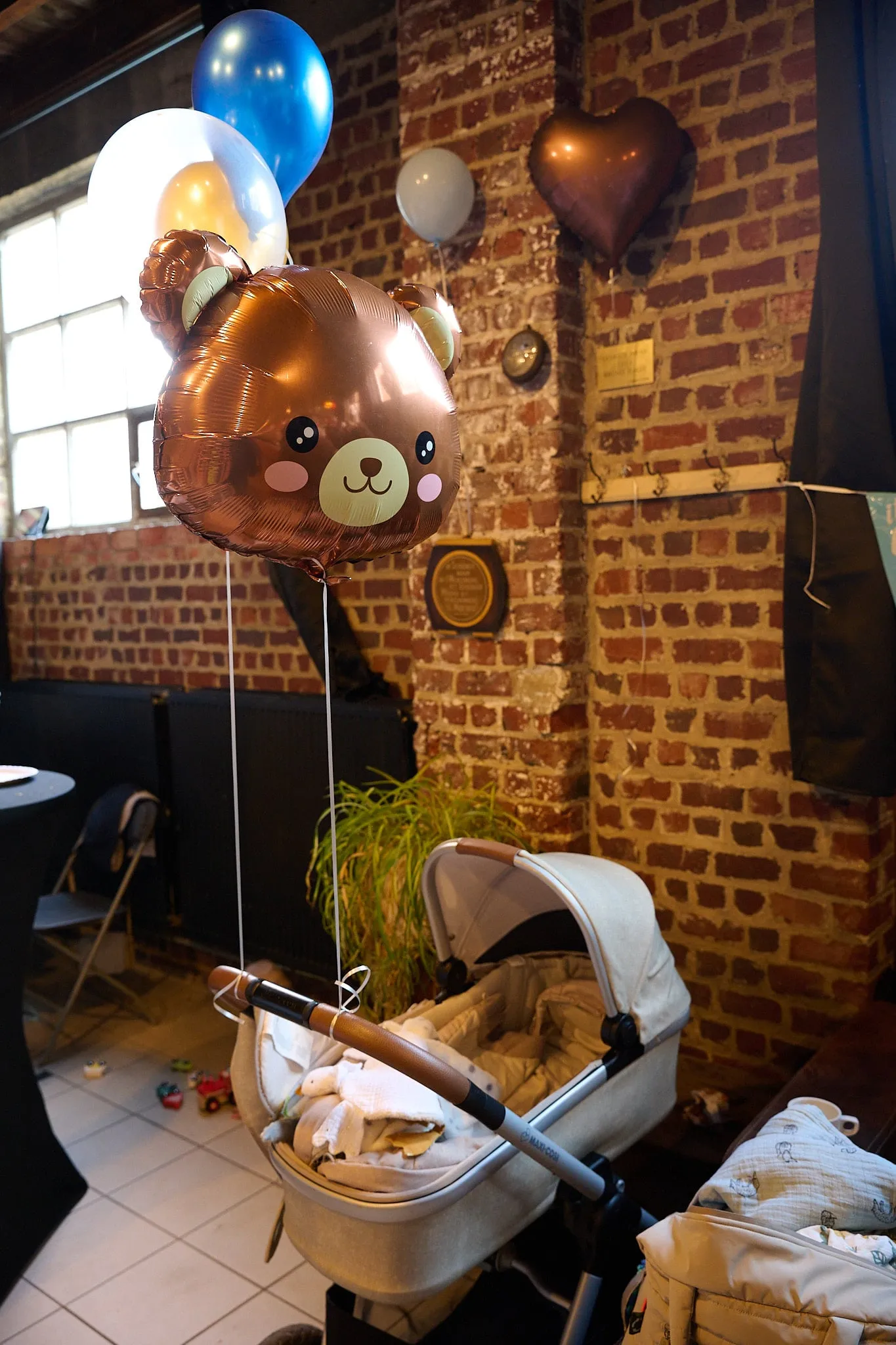Teddy bear balloon, balloons and a pram by a brick wall