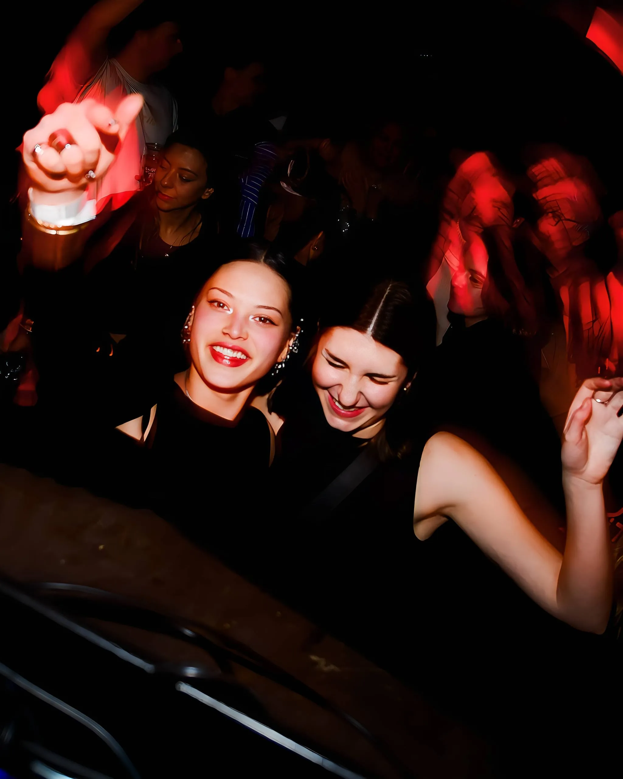 Two laughing women at a busy party, with motion blur