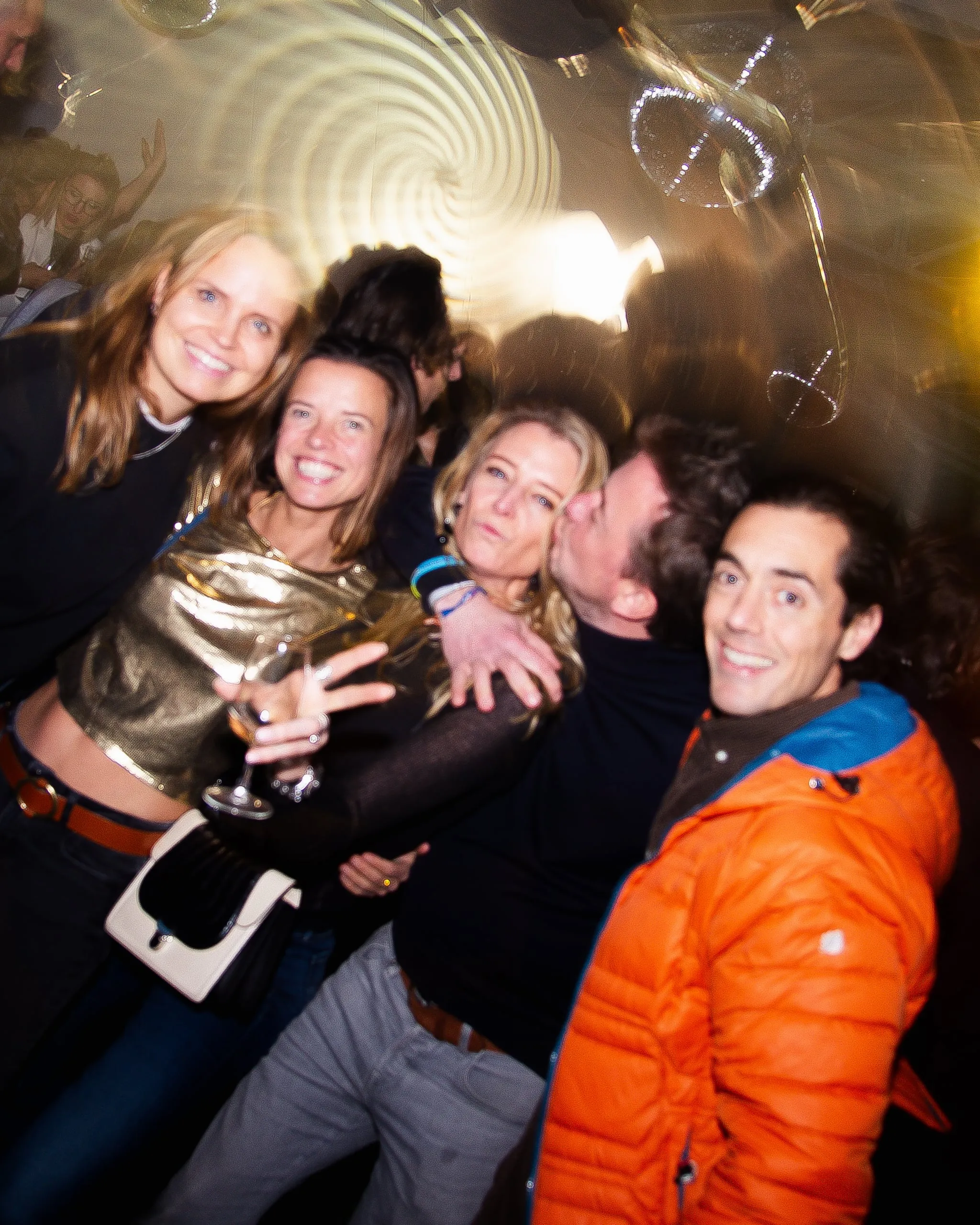Laughing friends pose together, one man wearing an orange jacket