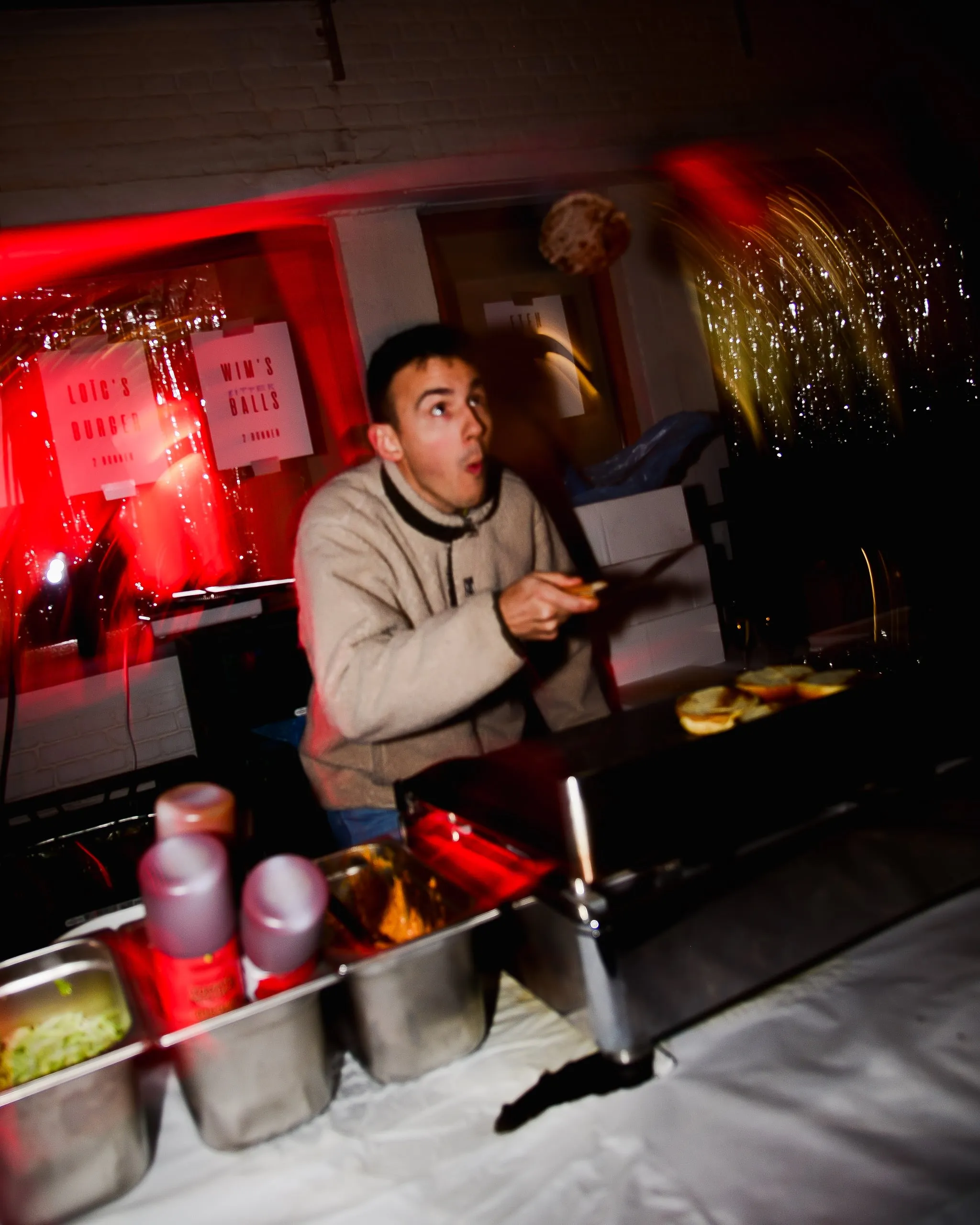 Man behind a food stand looks at the camera in surprise, in red light