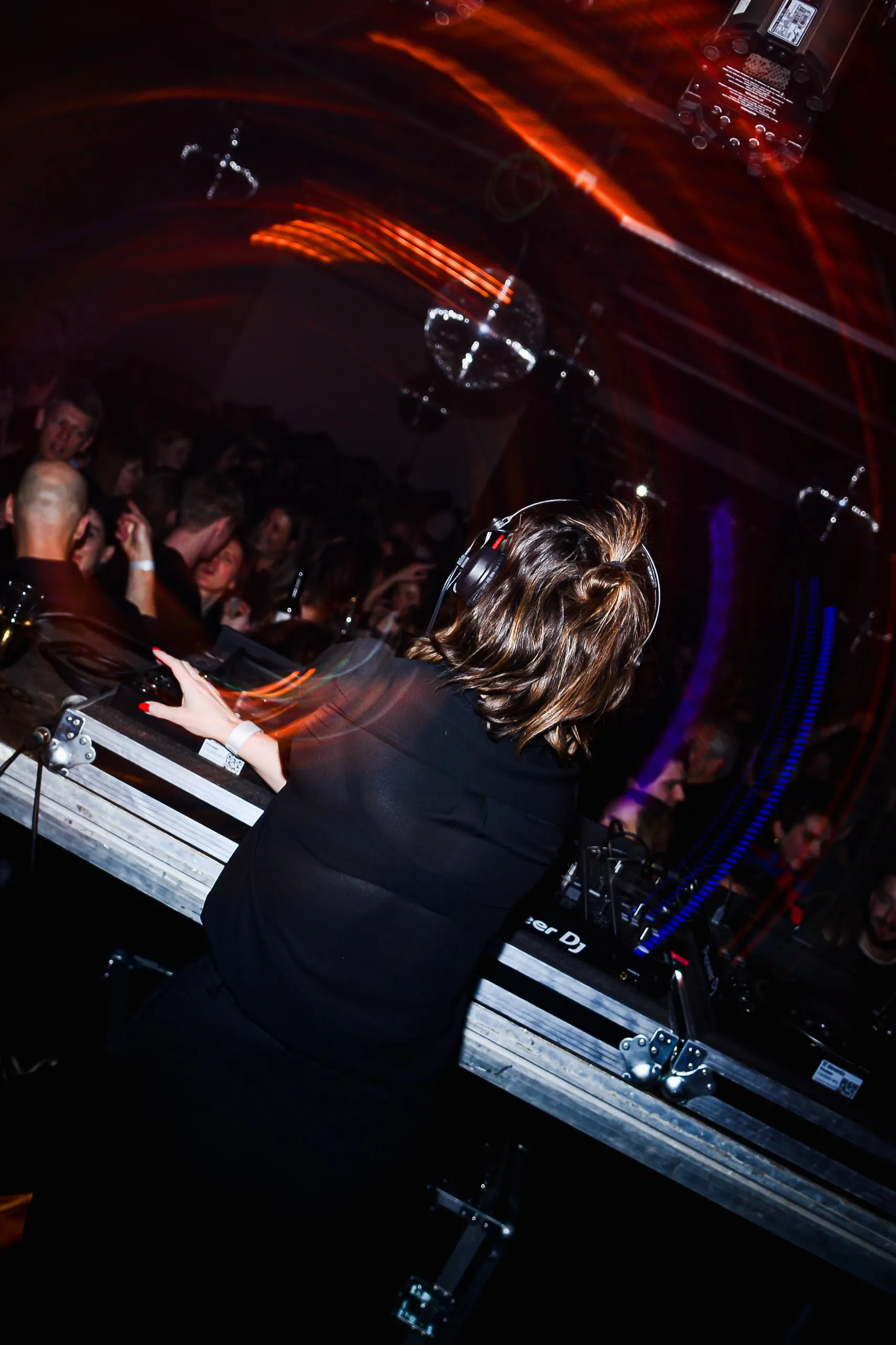 DJ behind the decks, seen from behind, with red light trails