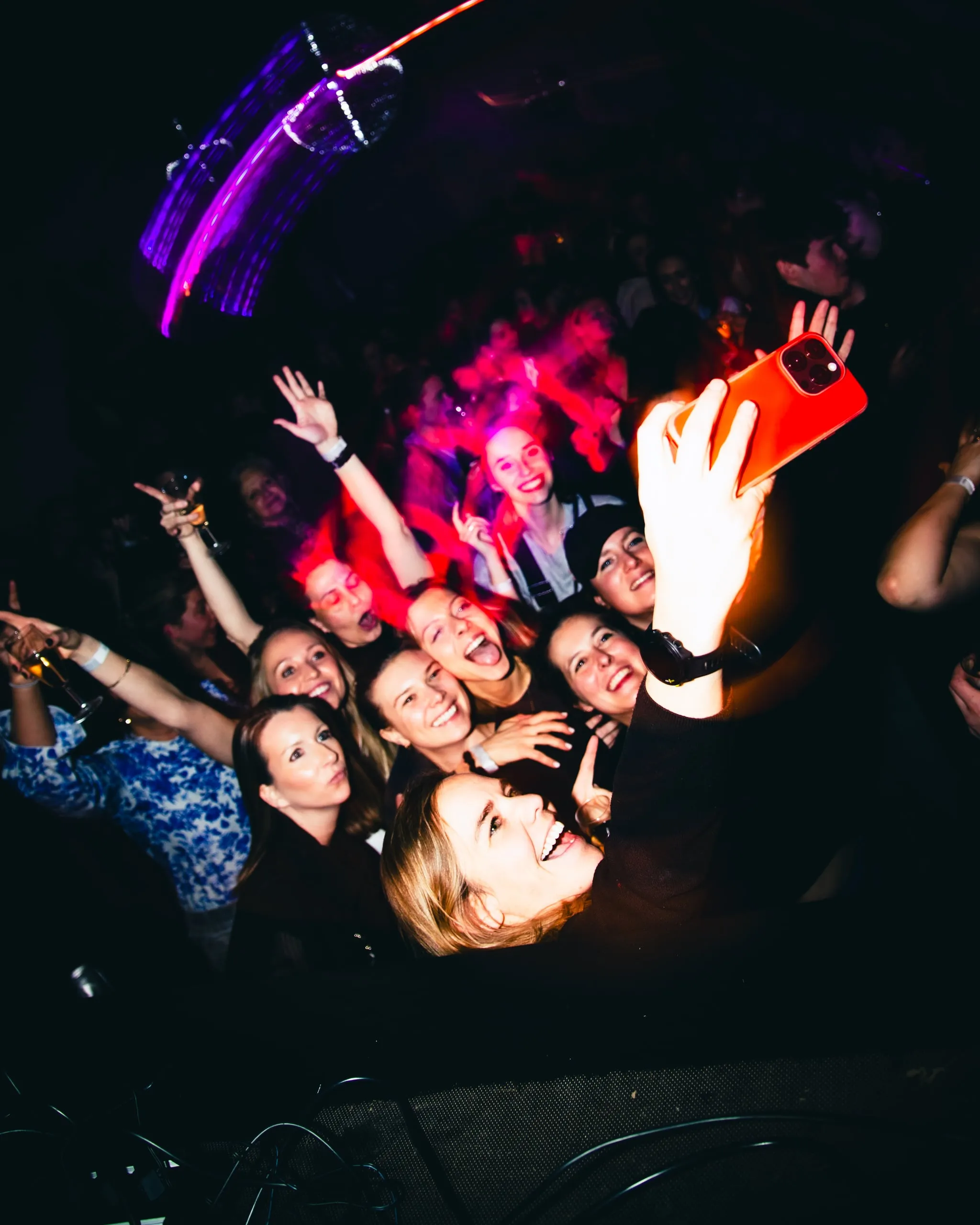 Partygoers take a selfie in a dark hall with red and purple light