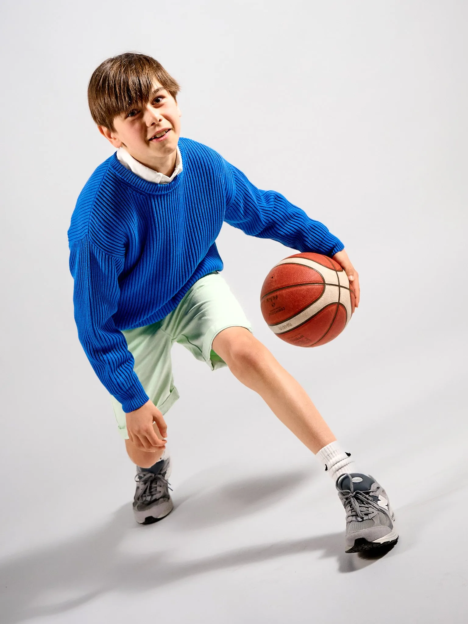 Boy in a blue sweater dribbling a basketball in the studio