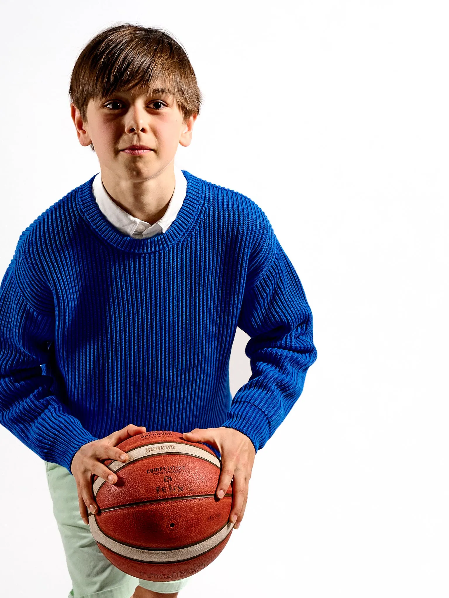 Boy in a blue sweater holding a basketball against a white background