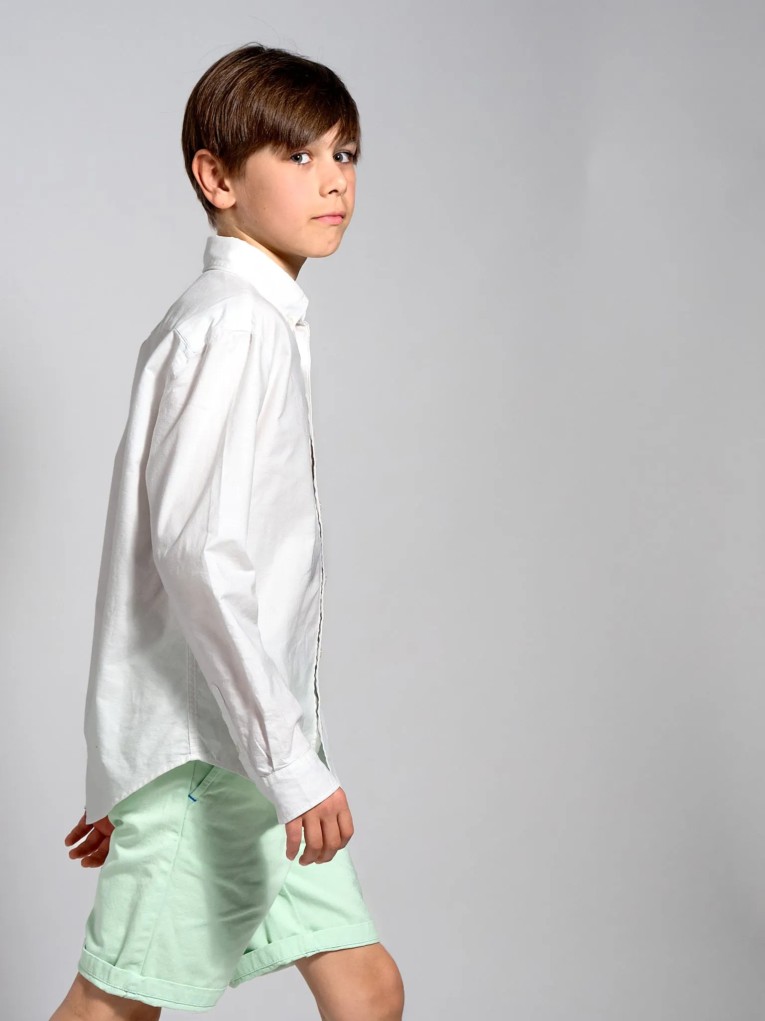 Boy in a white shirt and light green shorts walking in profile