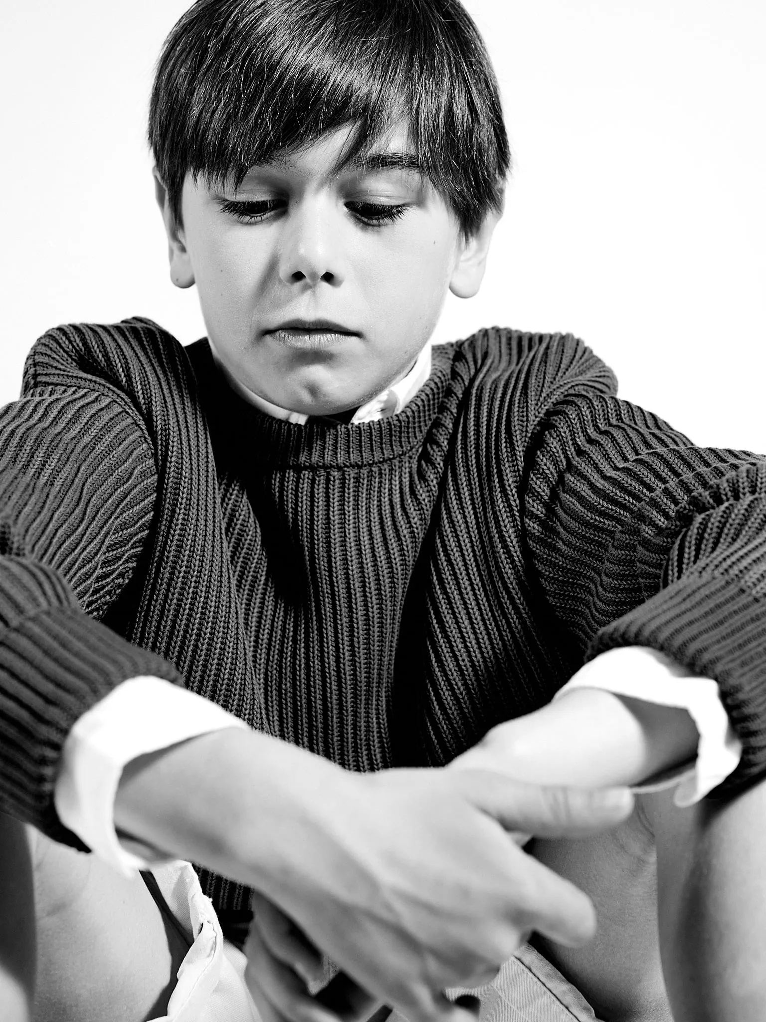 Black-and-white portrait of a boy looking down, with his arms around his knees