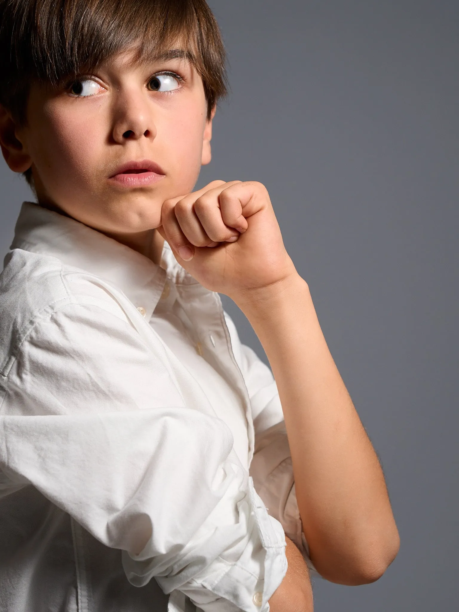Boy in a white shirt with a fist under his chin looking aside