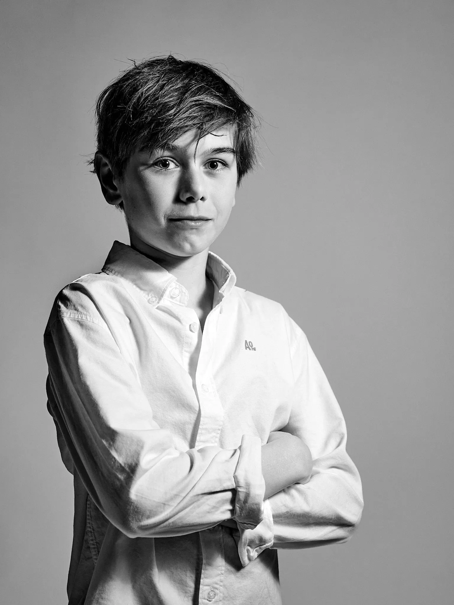 Black-and-white portrait of a boy in a white shirt with his arms crossed