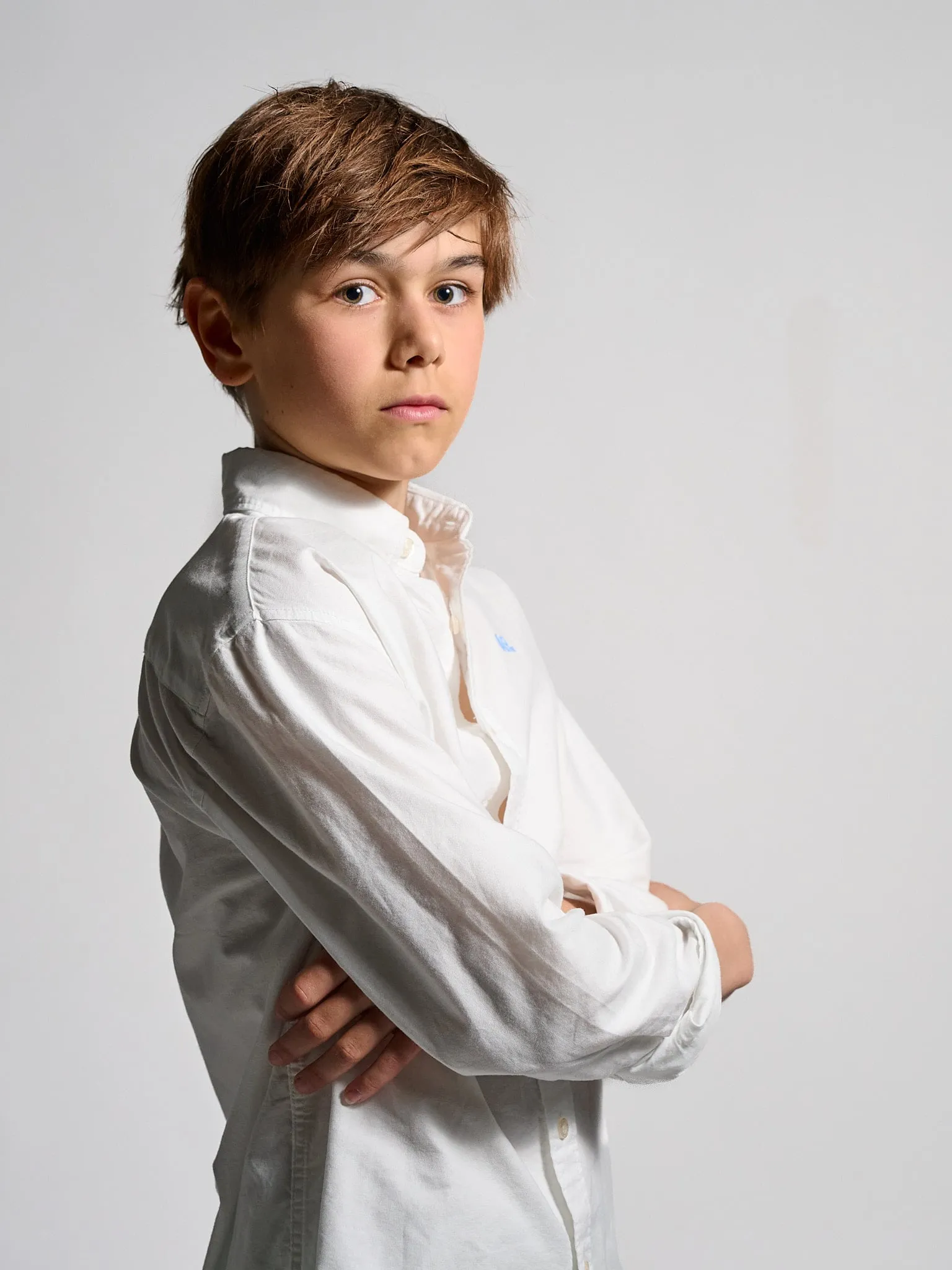 Boy in a white shirt with his arms crossed looking seriously at the camera