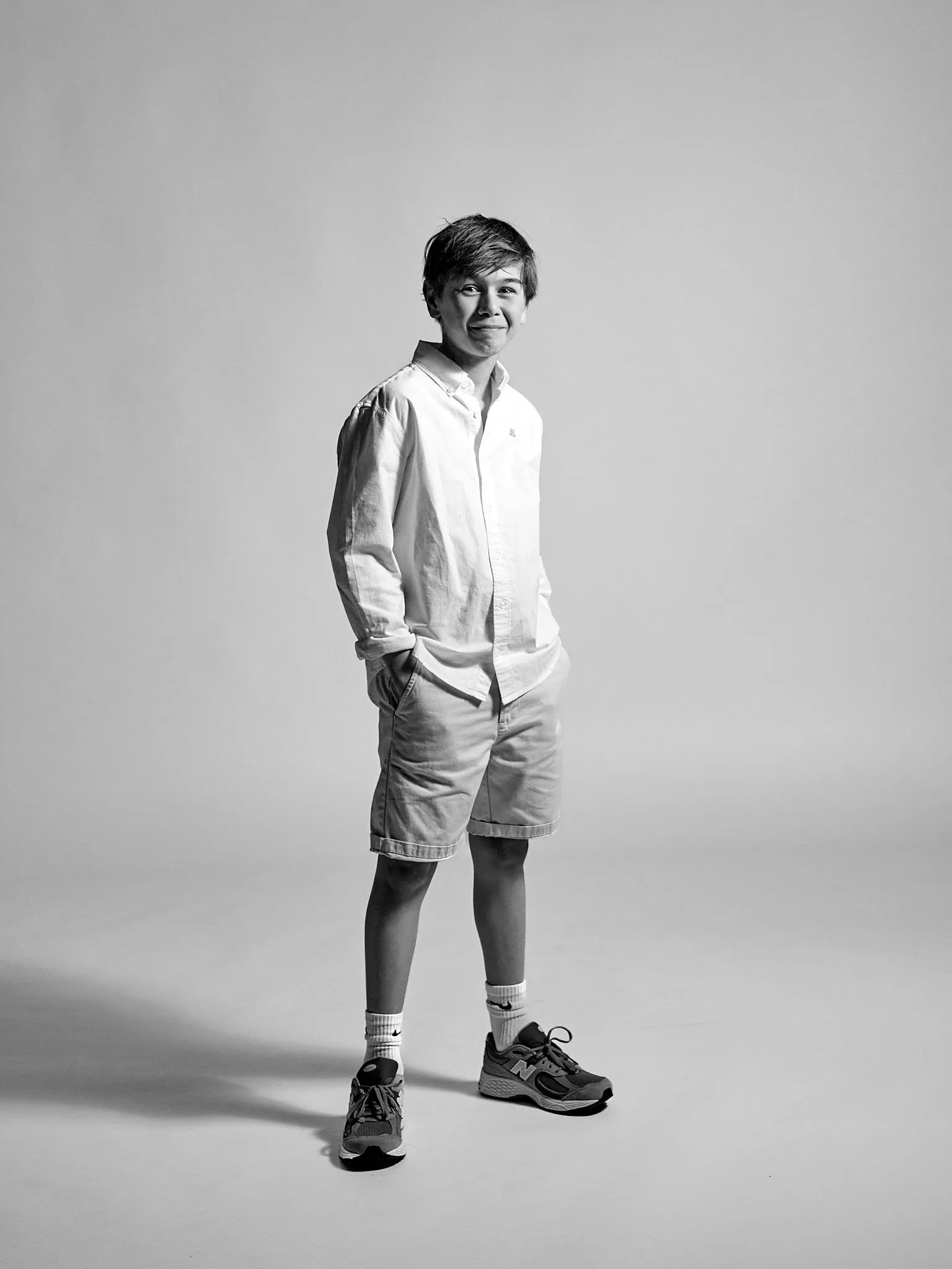 Black-and-white image of a smiling boy with his hands in his pockets