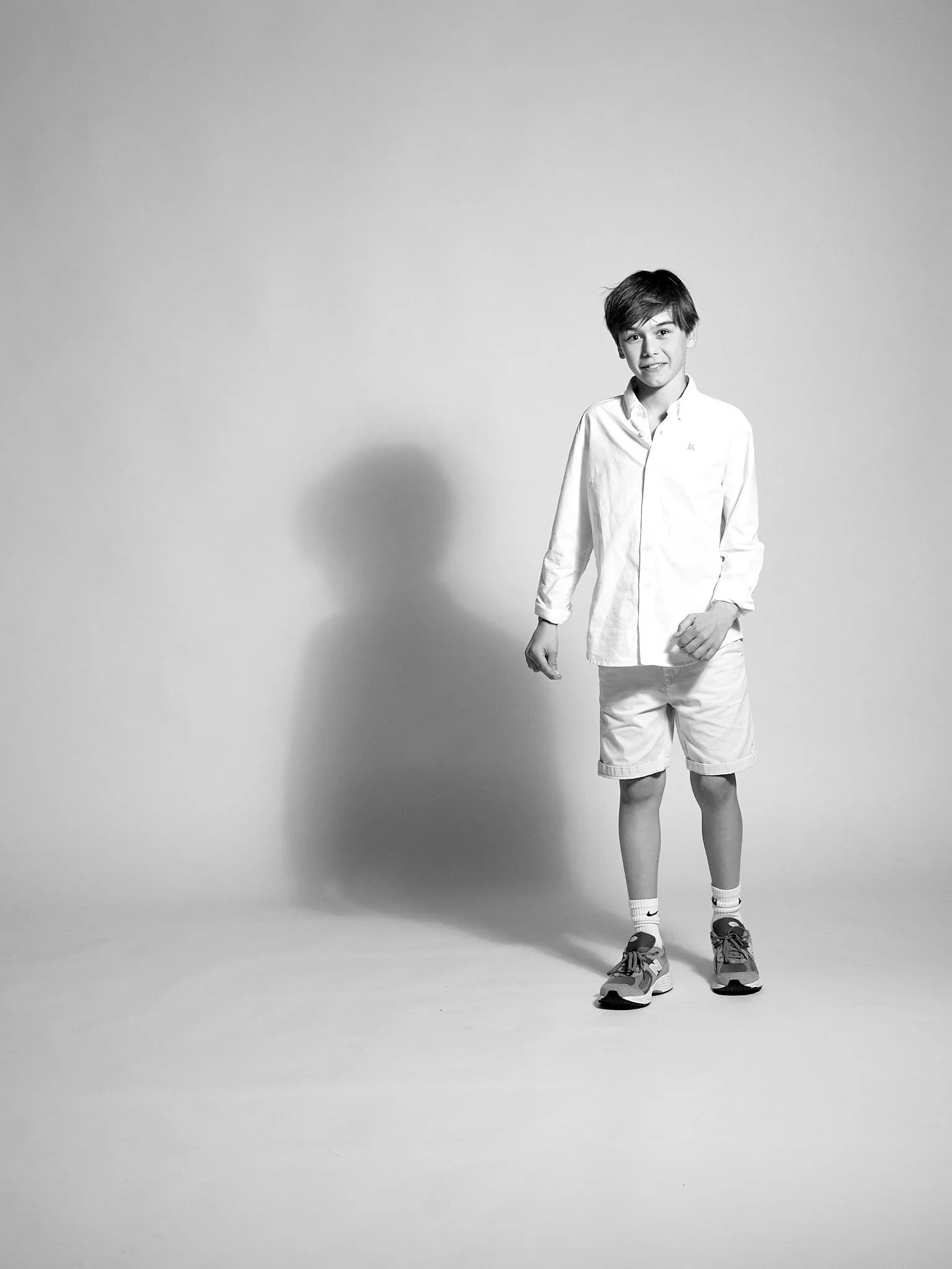 Black-and-white image of a boy in a white shirt with a long shadow in the background