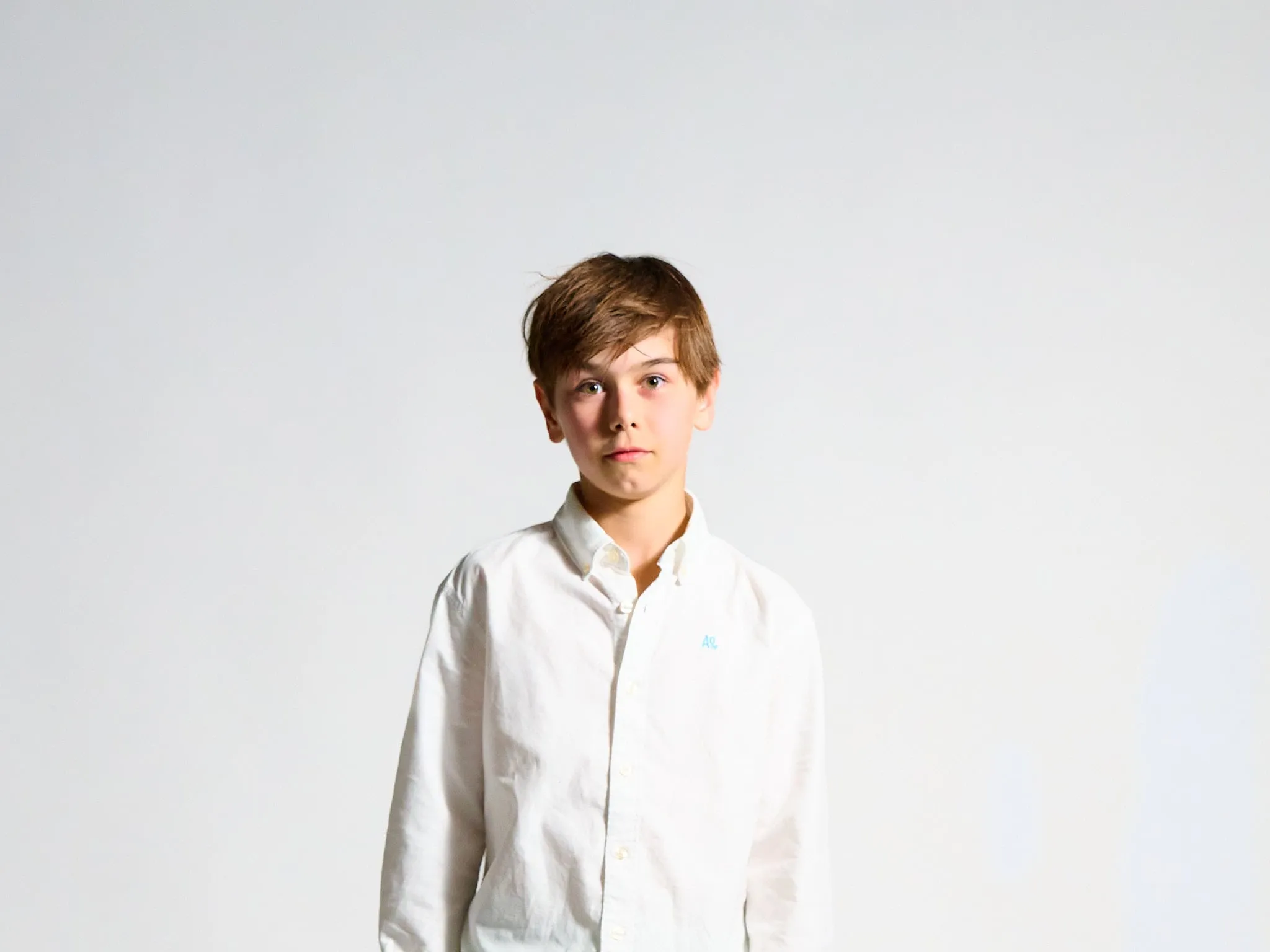 Boy in a white shirt looking seriously at the camera against a light background