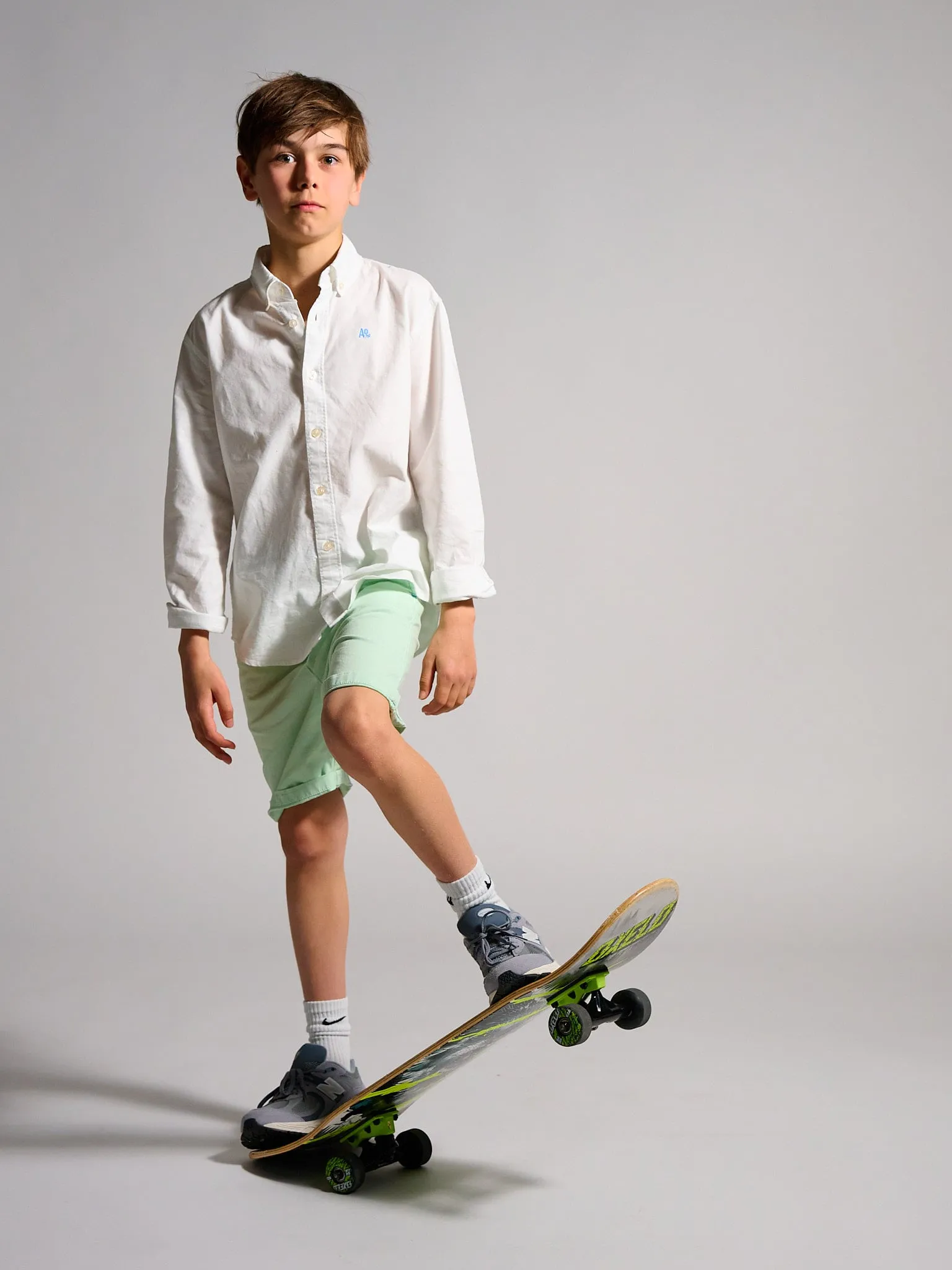 Boy in a white shirt and green shorts with a skateboard