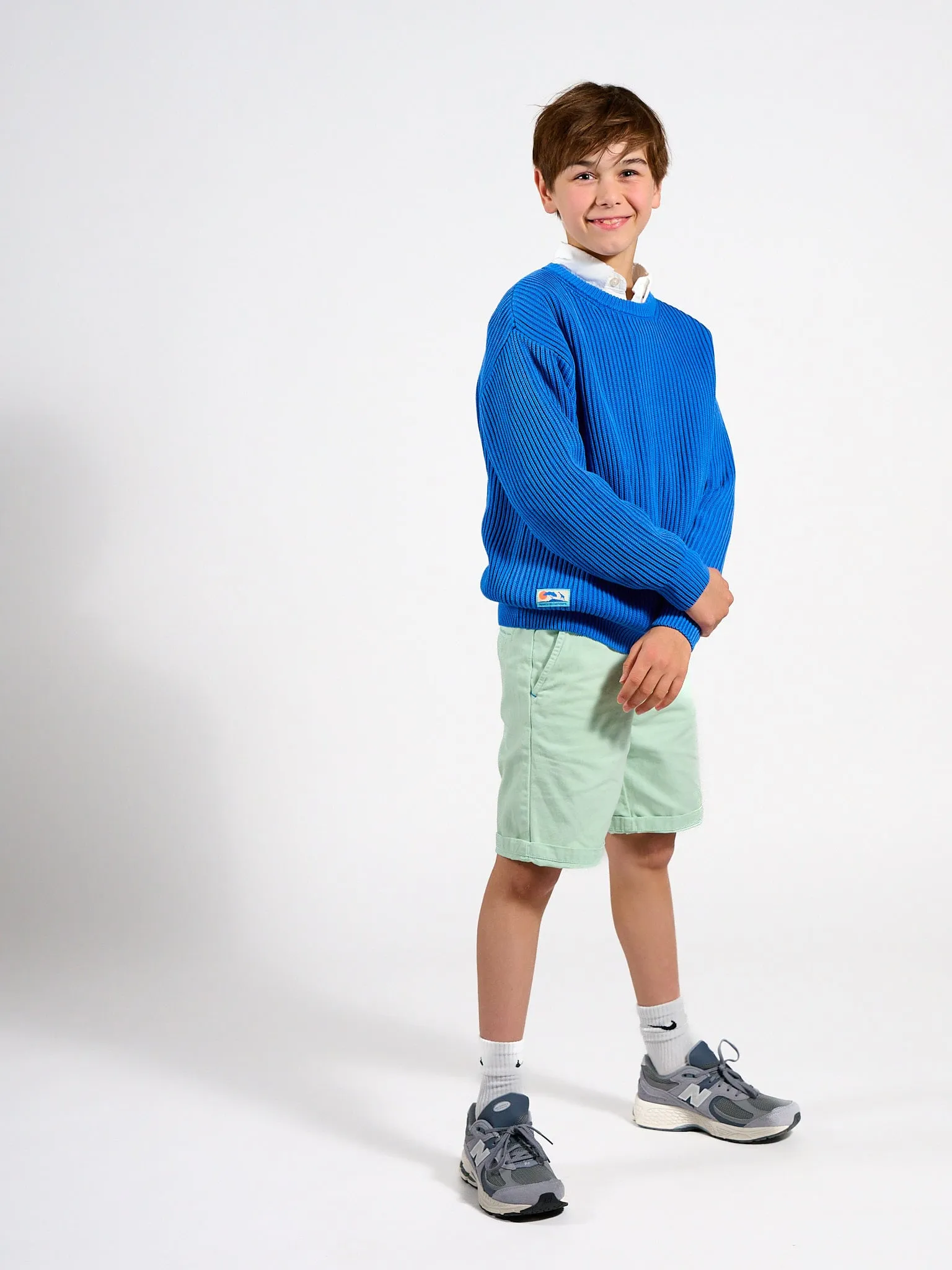 Smiling boy in a blue sweater and light green shorts, full length
