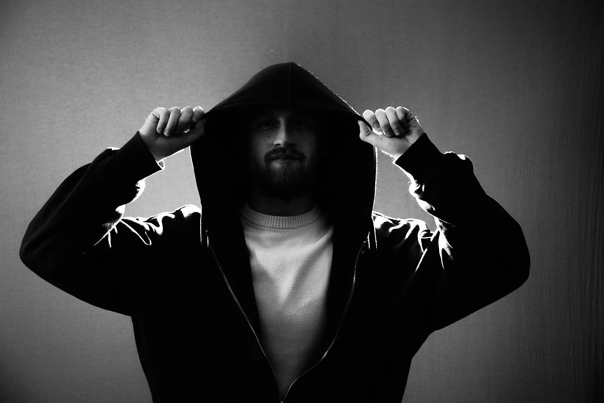 Man in a black hoodie pulling up the hood, with backlight, in black and white