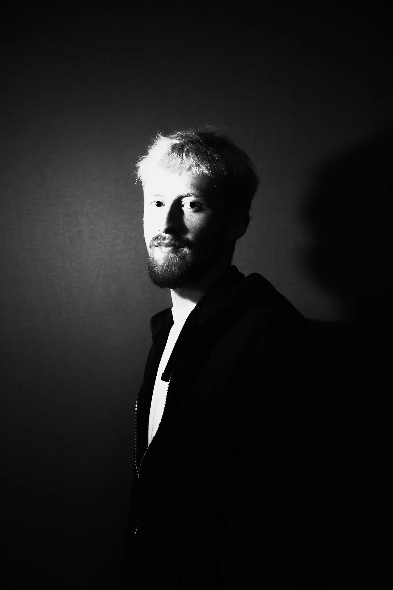 Man leans against a wall and looks into the camera, with hard side light