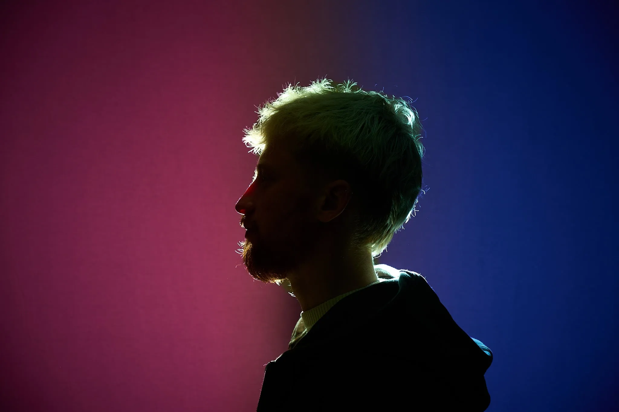 Profile of a man against a pink and blue lit background