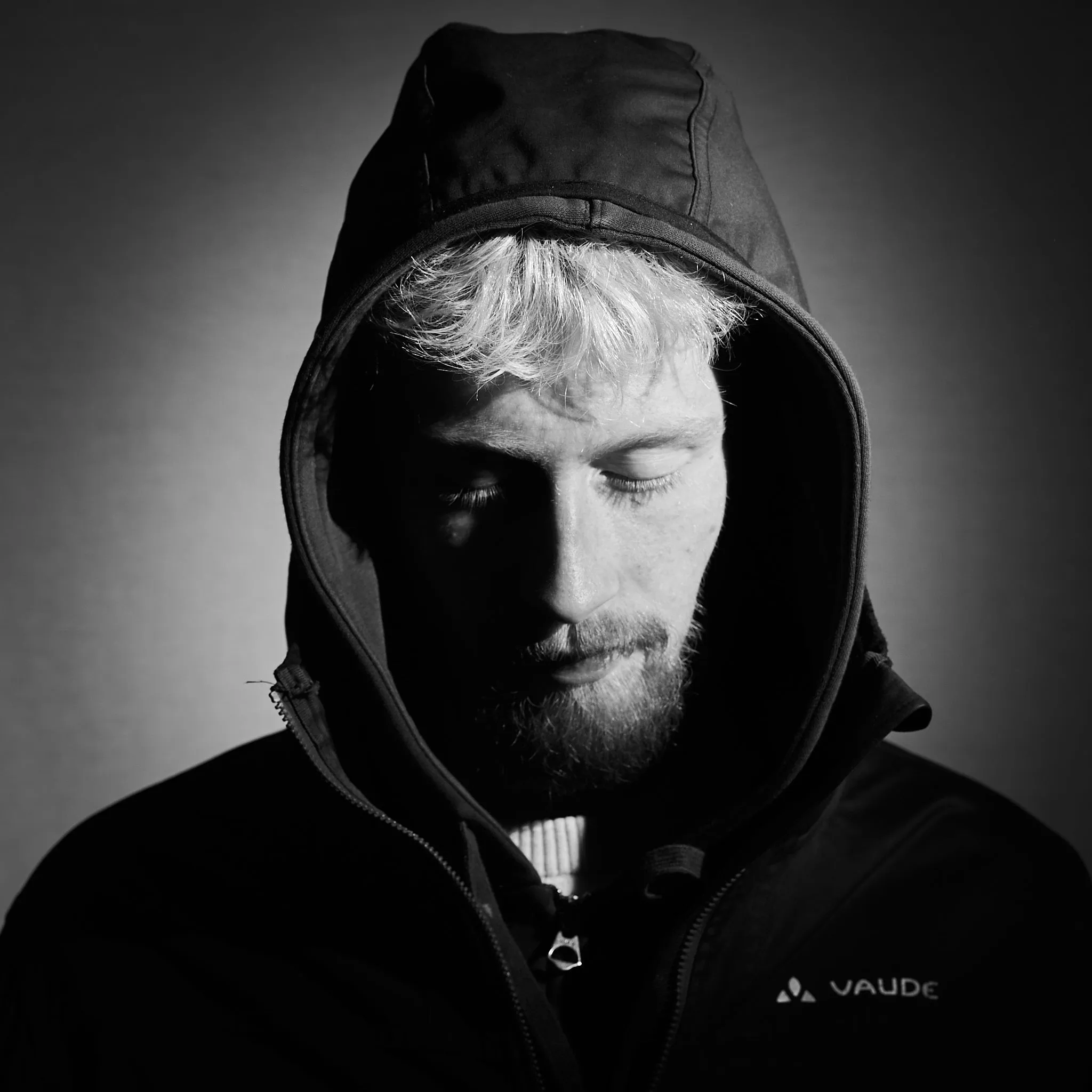 Black-and-white portrait of a man in a hood looking down