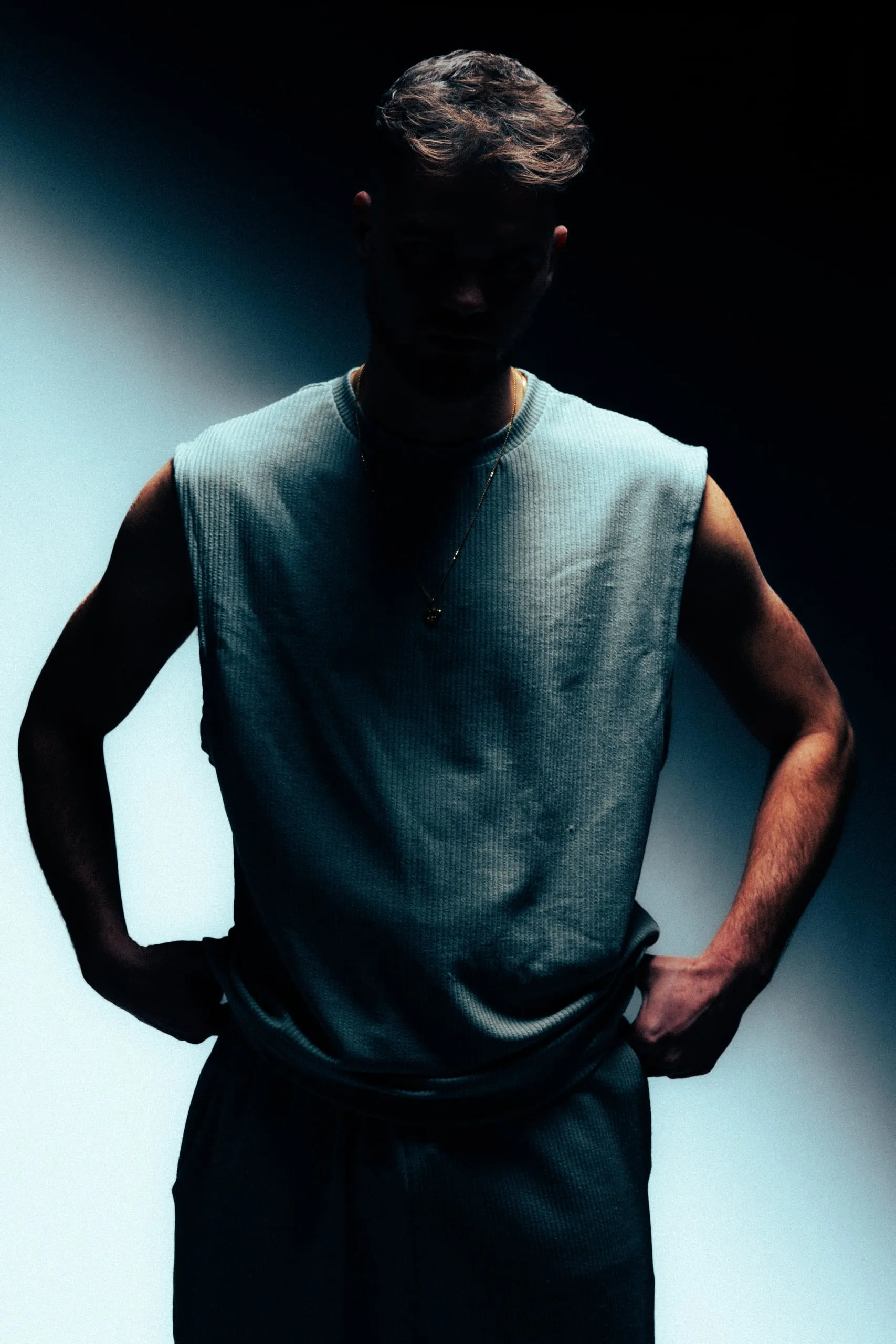 Man in a sleeveless shirt with his hands on his hips, his head in shadow