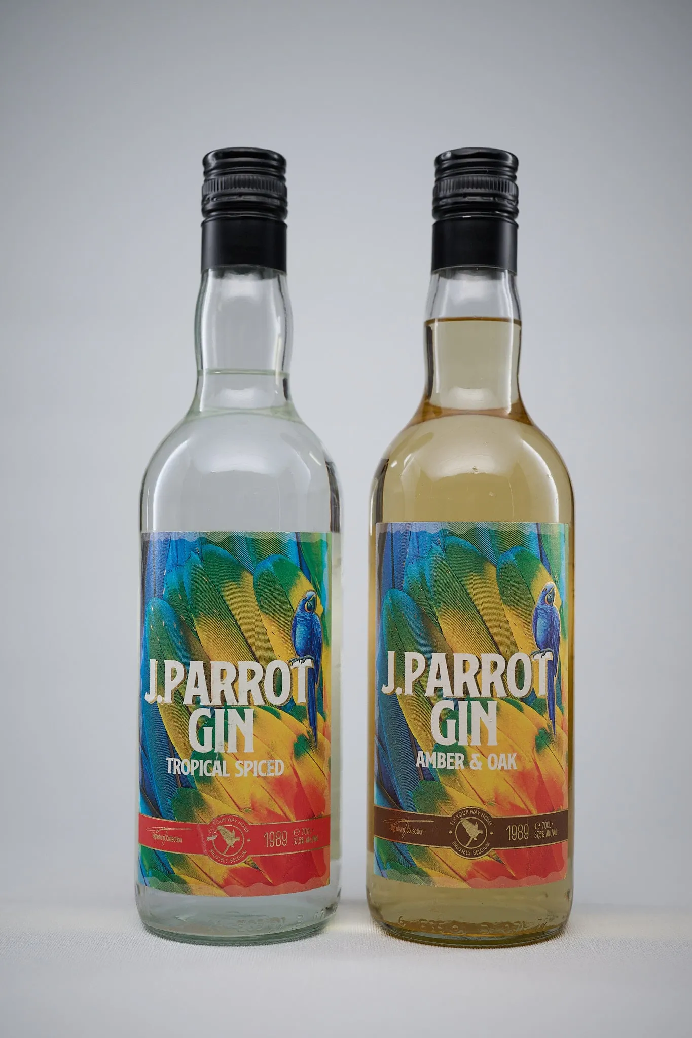 Two bottles of J. Parrot Gin (Tropical Spiced and Amber & Oak) against a light grey background