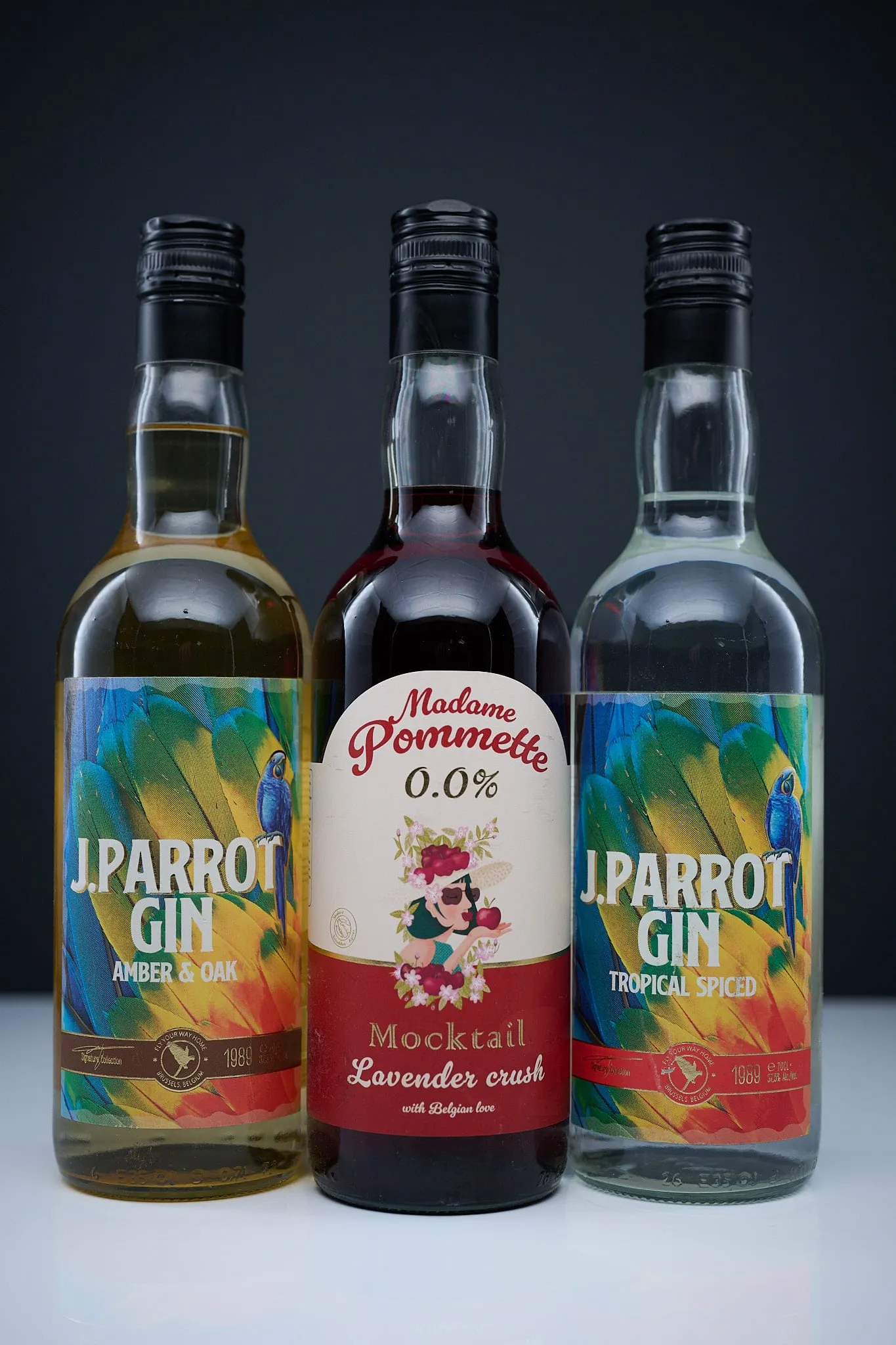 Three bottles of J. Parrot Gin and Madame Pommette side by side against a dark background