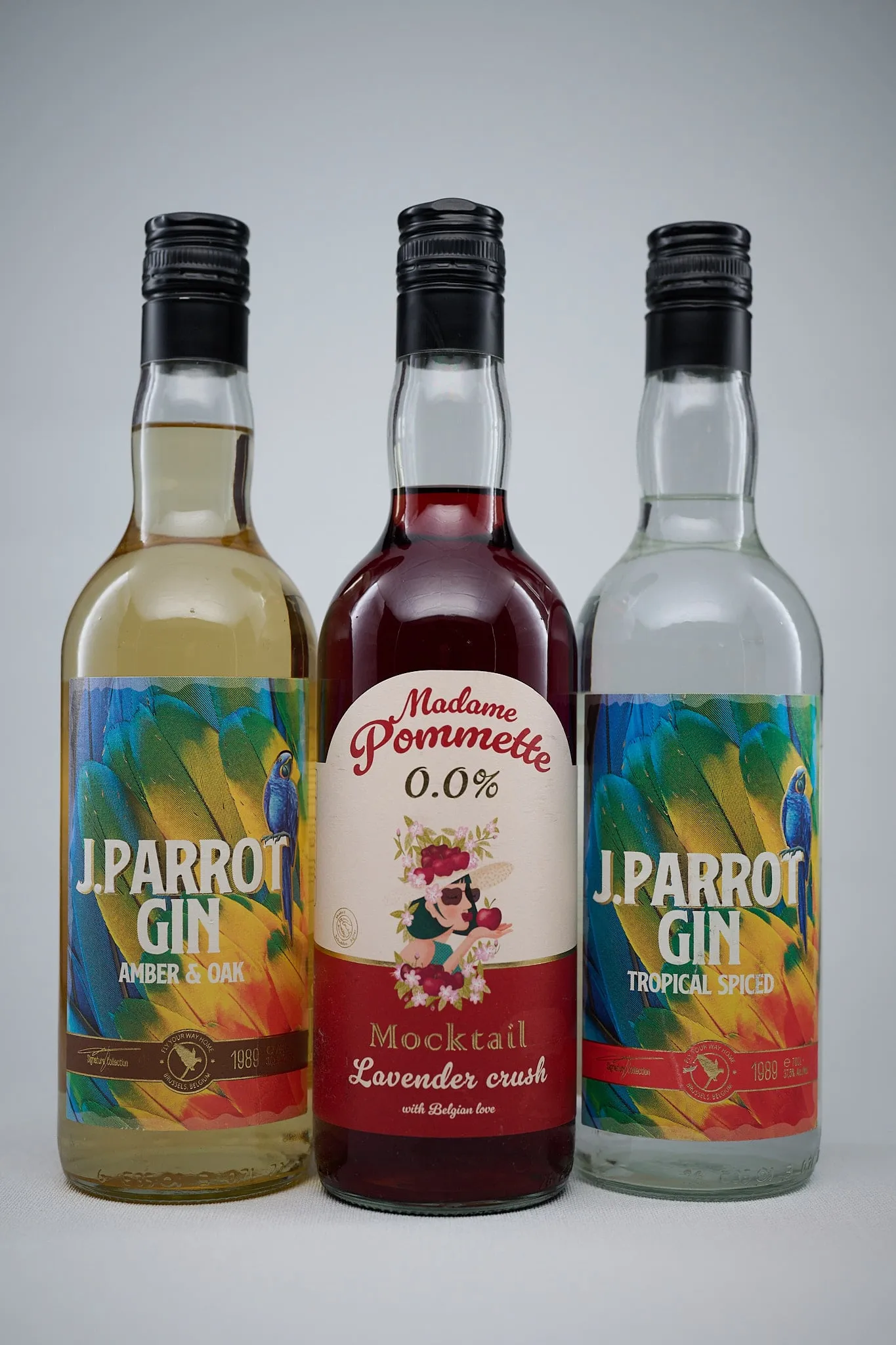 Three bottles of J. Parrot Gin and Madame Pommette against a light grey background