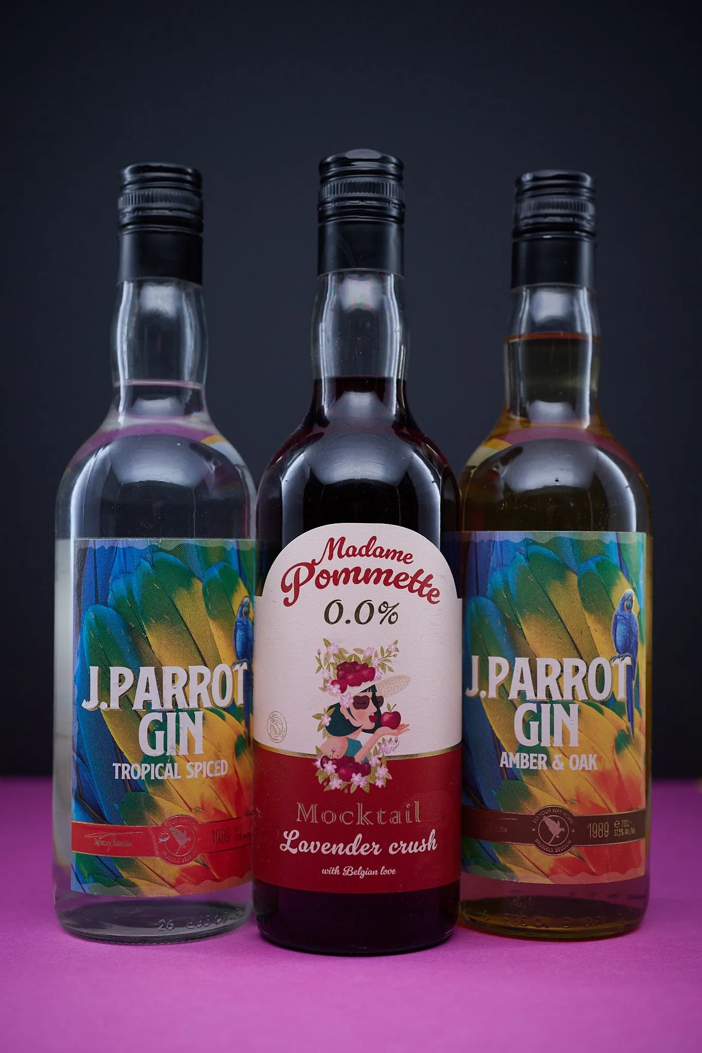 Three bottles of J. Parrot Gin and Madame Pommette side by side on a pink surface